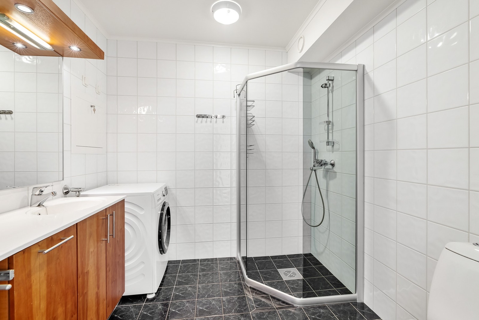 Innredning med heldekkende servant over innredning, høyskap, gulvstående toalett, dusjhjørne og opplegg for vaskemaskin. Galleribilde