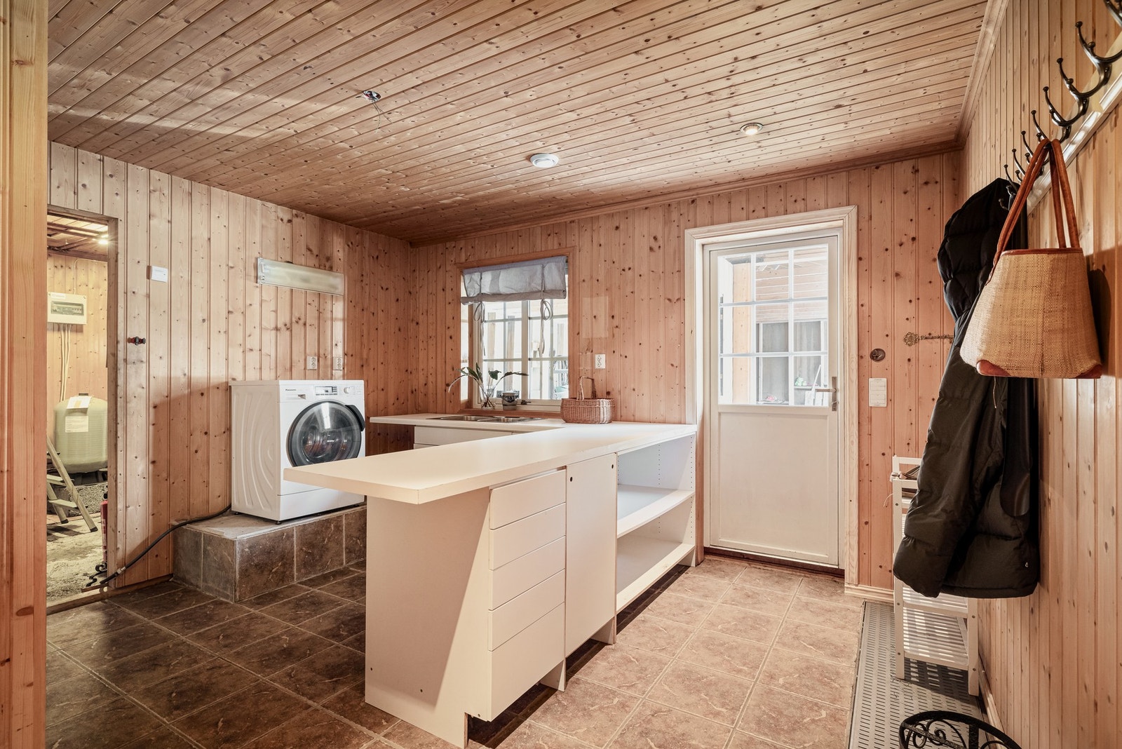 Romslig vaskerom med egen inngang - praktisk i hverdagen.
Terracottafargede fliser med gulvvarme og panelte vegger.
Opplegg for vaskemaskin og gode arbeidsflater. Galleribilde
