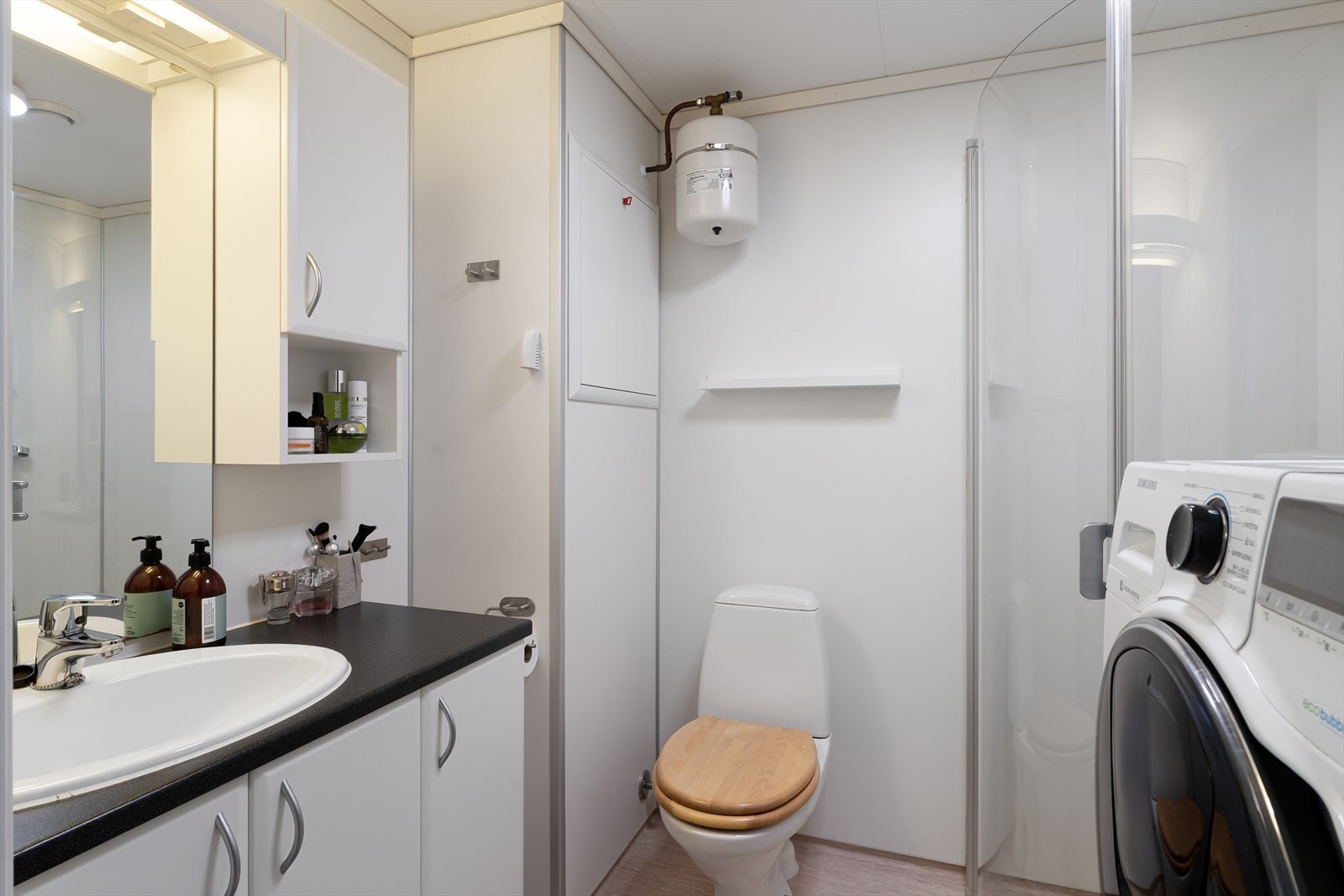 Lyst bad med baderomsplater på vegg og belegg på gulv. Opplegg til vaskemaskin og tørketrommel. Galleribilde
