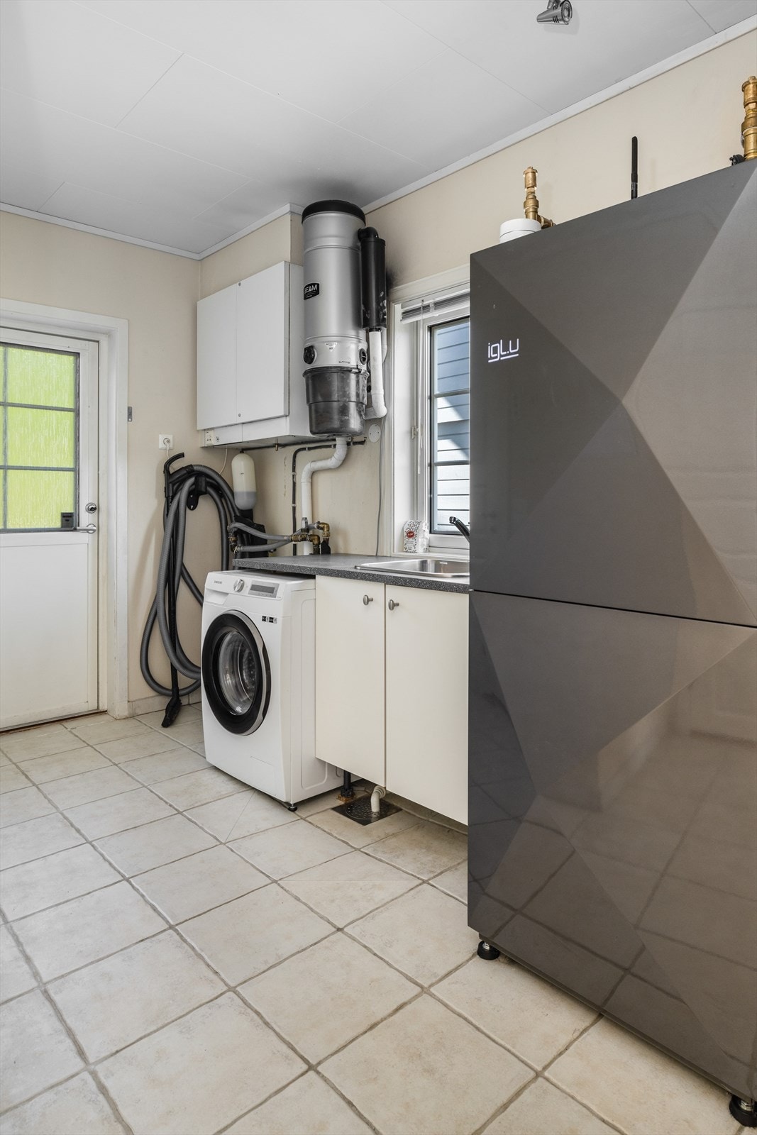 Med adkomst via skyvedør fra kjøkkenet kommer man inn på vaskerommet som er på 9,4 m2. Vaskerommet har også adkomst fra gårdsplassen. Her er det en praktisk løsning med benkeplate, opplegg til vaskemaskin. Den splitter nye vannvarmepumpen er plassert her. Galleribilde