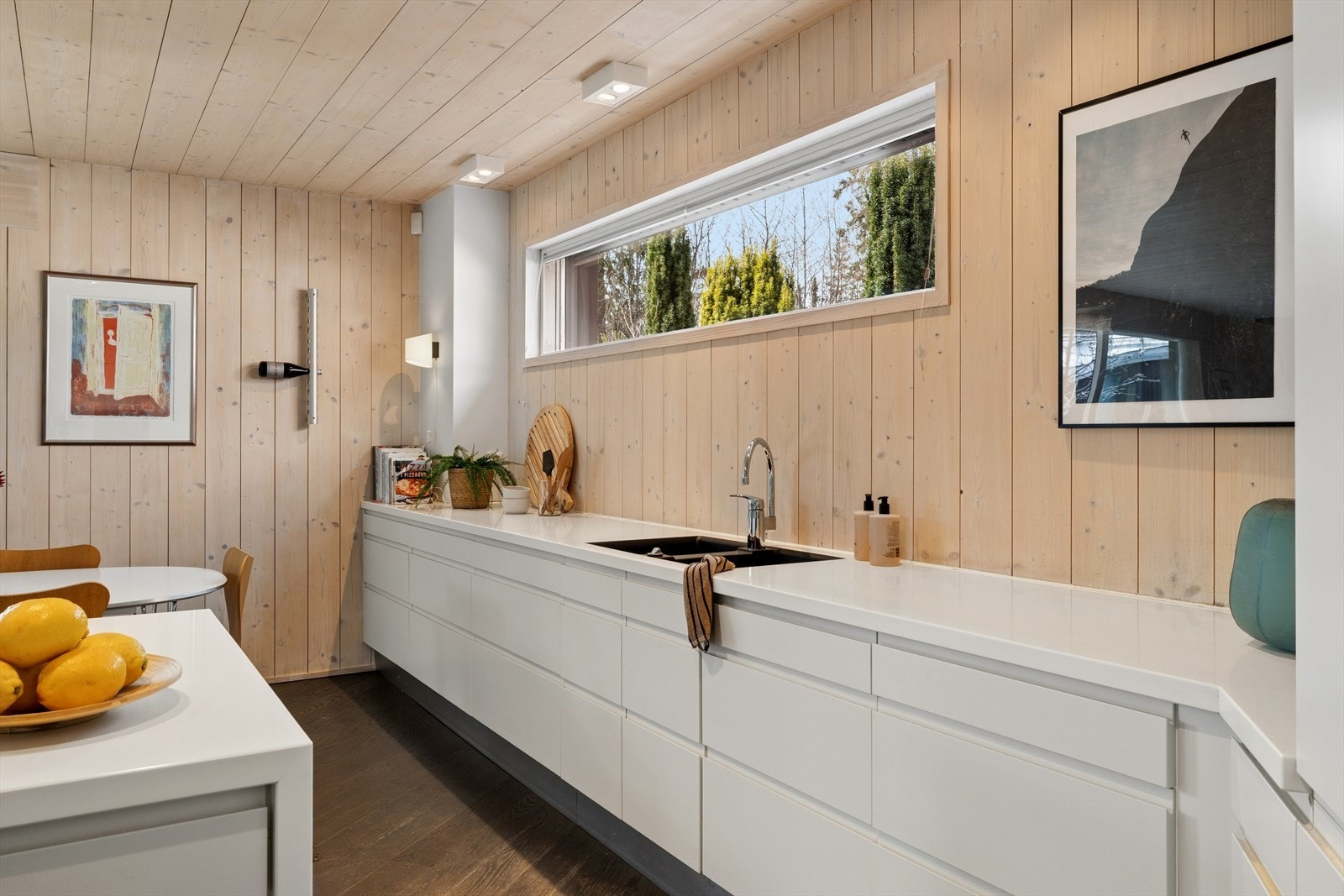 Innredningen har slette, lakkerte fronter i lys utførelse, kombinert med en stilren benkeplate i komposittmateriale (Corian/Dekton). Galleribilde