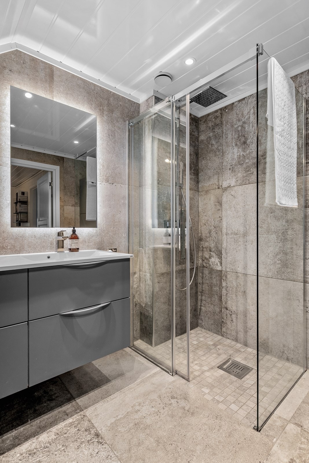 Badet er utstyrt med flis på gulv og vegger. Malt overflate i himling. Gulvvarme. tstyrt med dusjhjørne, servantskap, veggmontert wc og mekanisk avtrekk Galleribilde