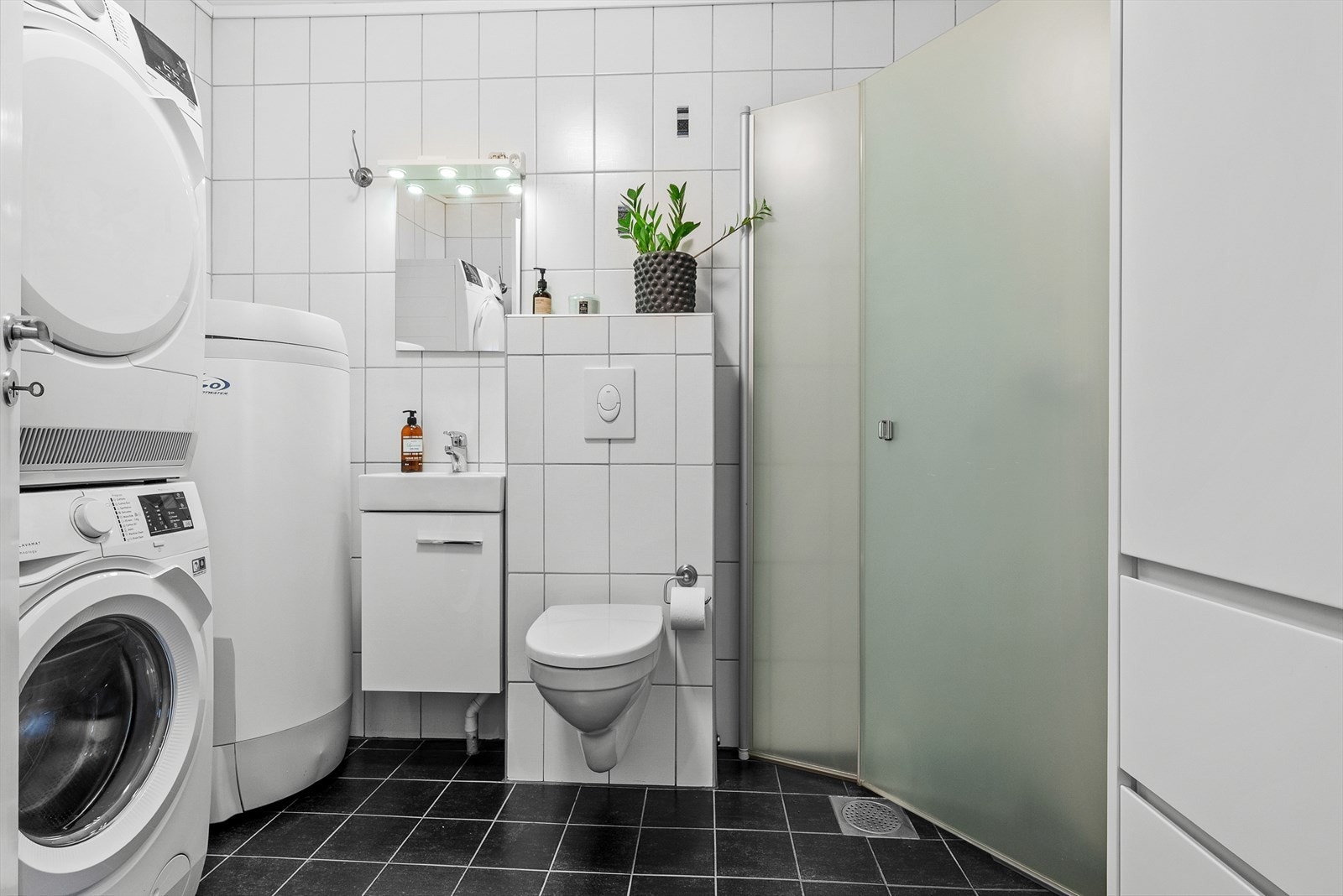 Badet på hovedplan er praktisk innredet med flis på gulv, flis og malt overflate på vegger. Takess i himling. Gulvvarme. Utstyrt med innfellbare dusjdører, servantskap, wc, opplegg for vaskemaskin og naturlig avtrekk. Galleribilde