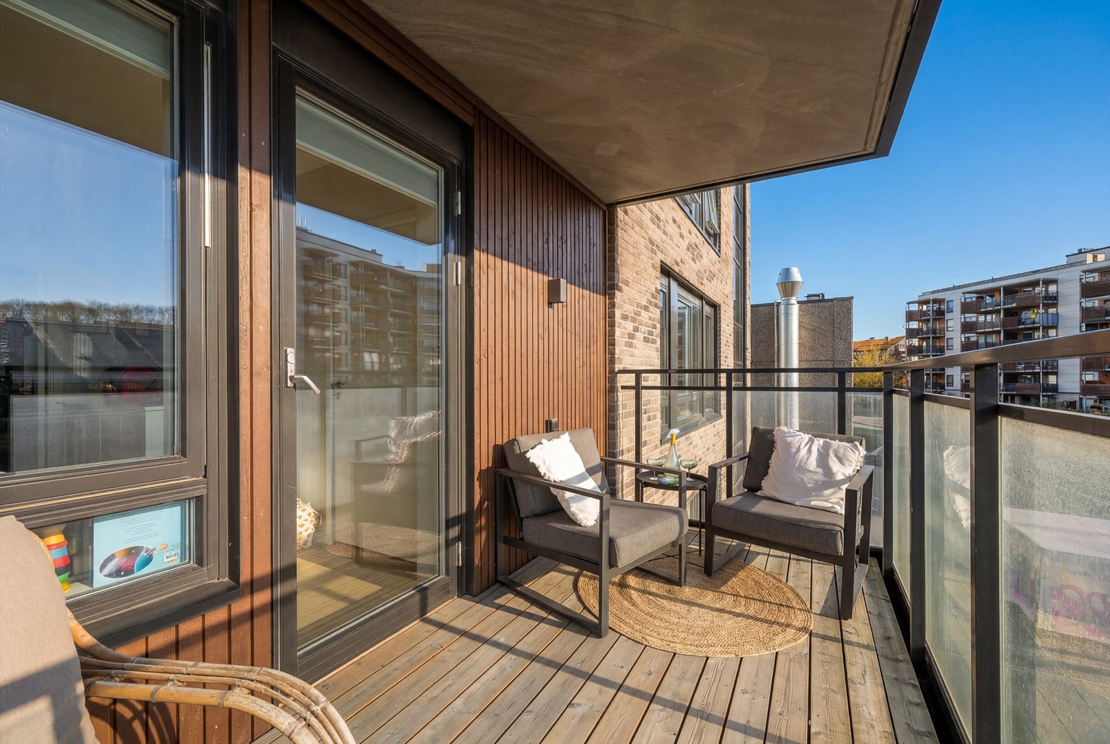 Balkongen har terrassebord på gulvet og rekkverk i glass. Galleribilde