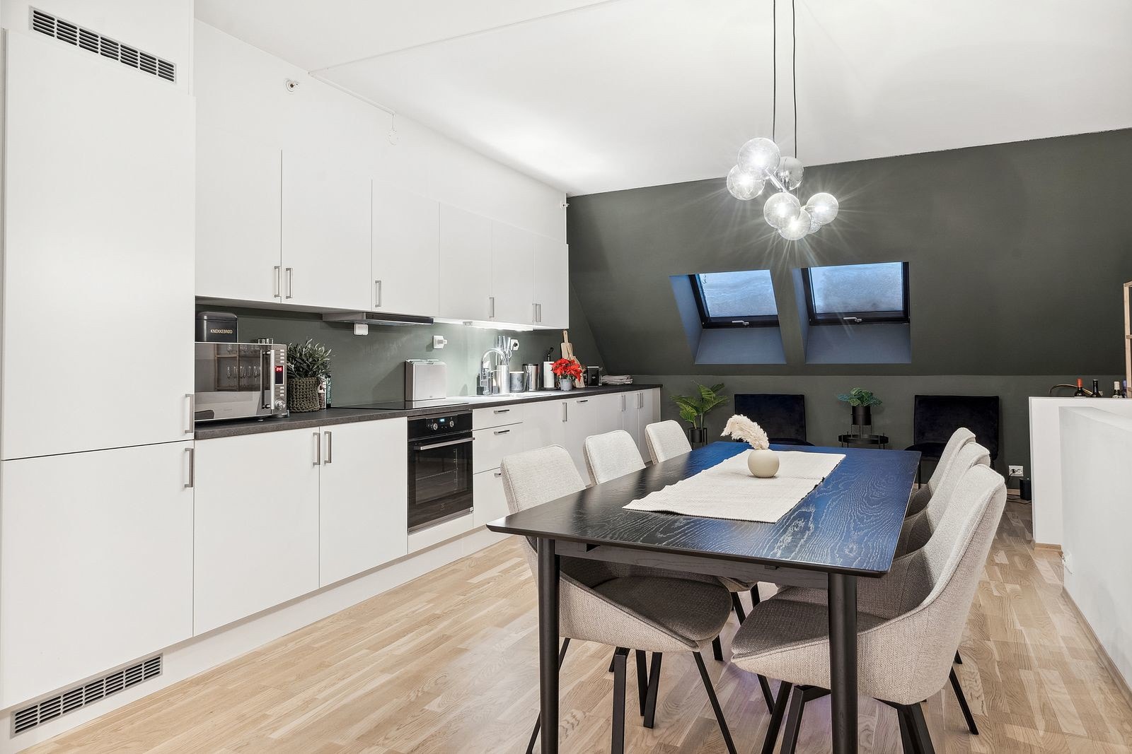 Åpen stue/kjøkkenløsning med moderne kjøkken med hvite fronter og integrerte hvitevarer.