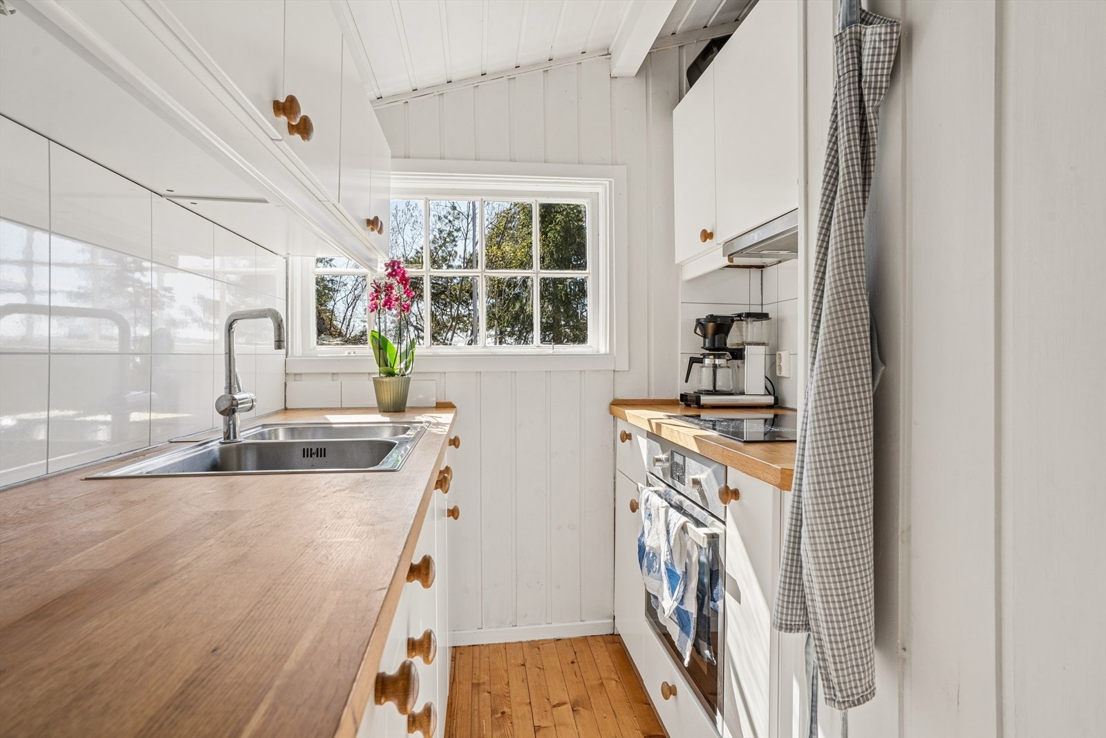 Kjøkken fra IKEA er utstyrt med hvit glatt kjøkkeninnredning, heltrebenkeplate, plater over benk, 2-kums utslagsvask med blandebatteri og kjøkkenventilator. Integrerte hvitevarer som komfyr og platetopp. Galleribilde