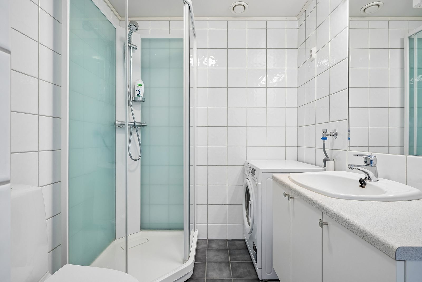 Flislagt bad med dusjkabinett og opplegg for vaskemaskin.