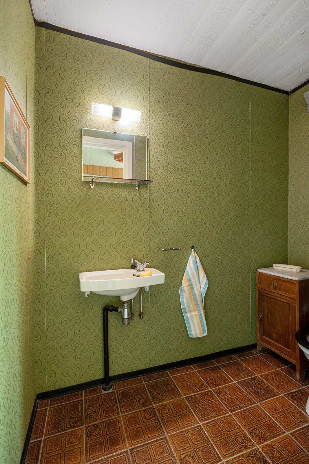 I hendig tilknytning til entreen det et separat wc-rom med tapetserte vegger og fliser på gulv med vannbåren gulvvarme. I tillegg til et gulvmontert toalett har rommet en servant og et speil med hylle. Galleribilde