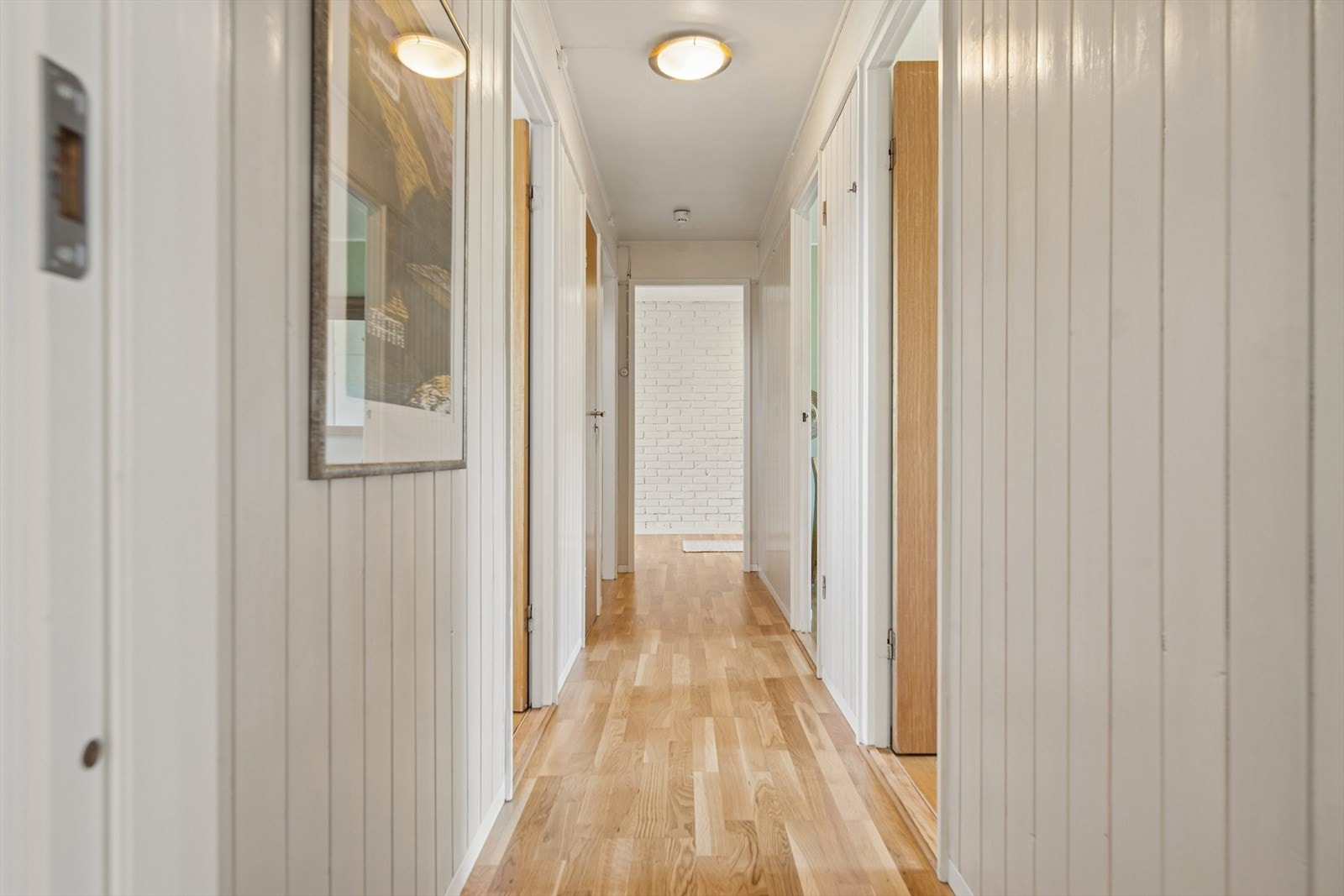 Gjennomgående parkett og lyse panelvegger skaper en helhetlig stil i gangen. Galleribilde