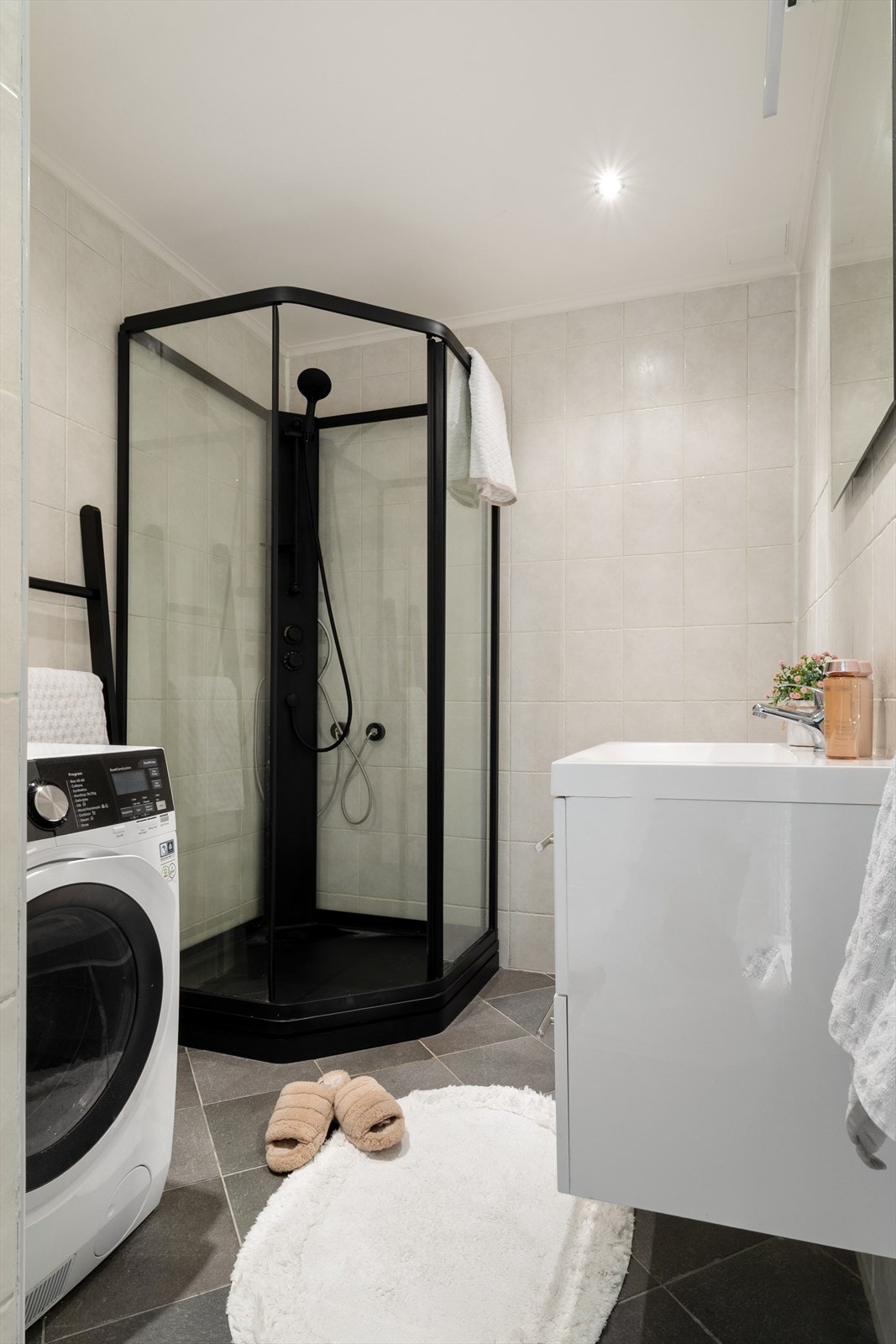 Badet har opplegg til vaskemaskin. Dusjkabinett i sorte detaljer. Galleribilde
