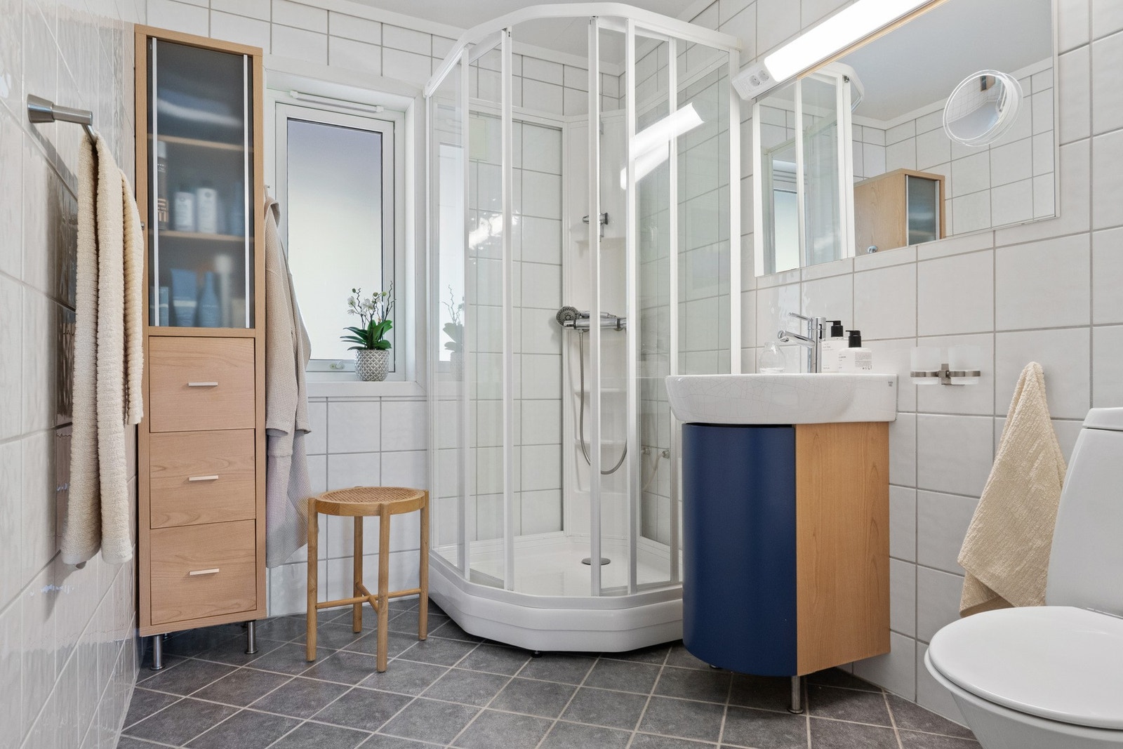 Hovedbadet ligger i på hovedplan i nær tilknytning til soverommene. Det er lyst og innbydende med tidløst uttrykk, lyse fliser på vegger som gir en ren og moderne følelse, kombinert med mørke gulvfliser som skaper en elegant kontrast. Galleribilde