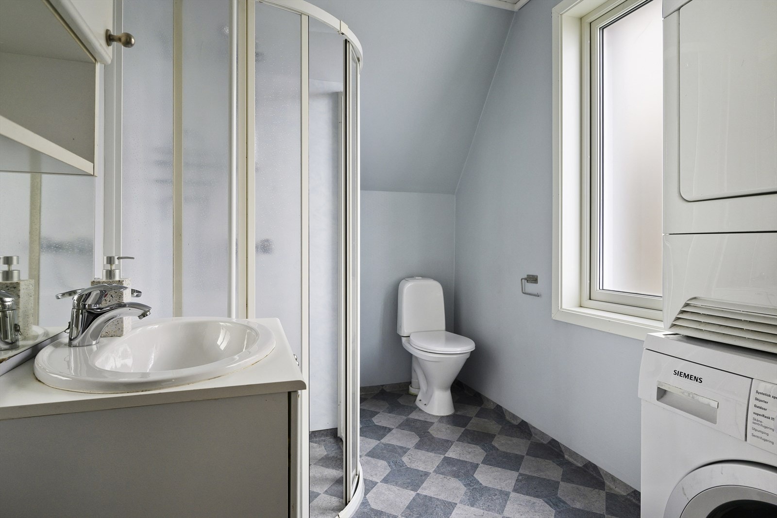 Bad som har innredning med servant nedfelt i servantskap, veggskap, speil, toalett, dusjvegger/hjørne og opplegg/plass for vaskemaskin og kondenstørketrommel. Galleribilde