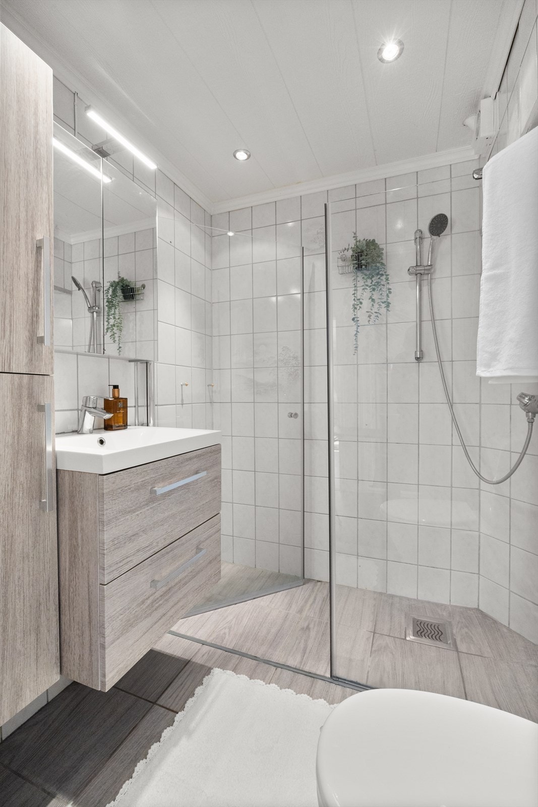 Badet er innredet med gulvstående klosett, baderomsinnredning med heldekkende servant, speilskap og dusjvegger. Galleribilde
