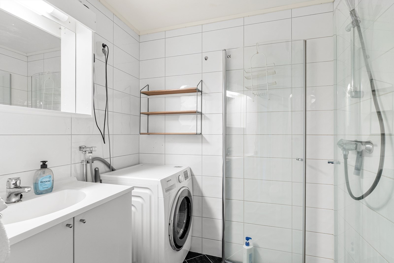 Lyst bad med varmekabler i gulv. Badet er utstyrt med dusjhjørne, toalett, lys baderomsinnredning og opplegg for vaskemaskin. Galleribilde