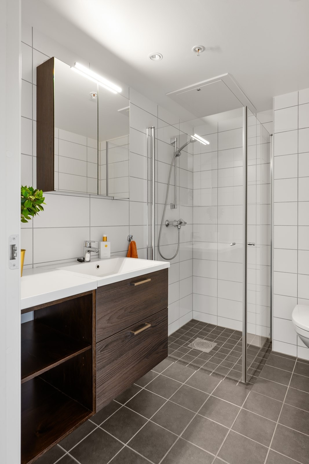 Badet er utstyrt med vegghengt toalett, dusjhjørne med innsvingbare glassdører og baderomsinnredning med servant. Galleribilde