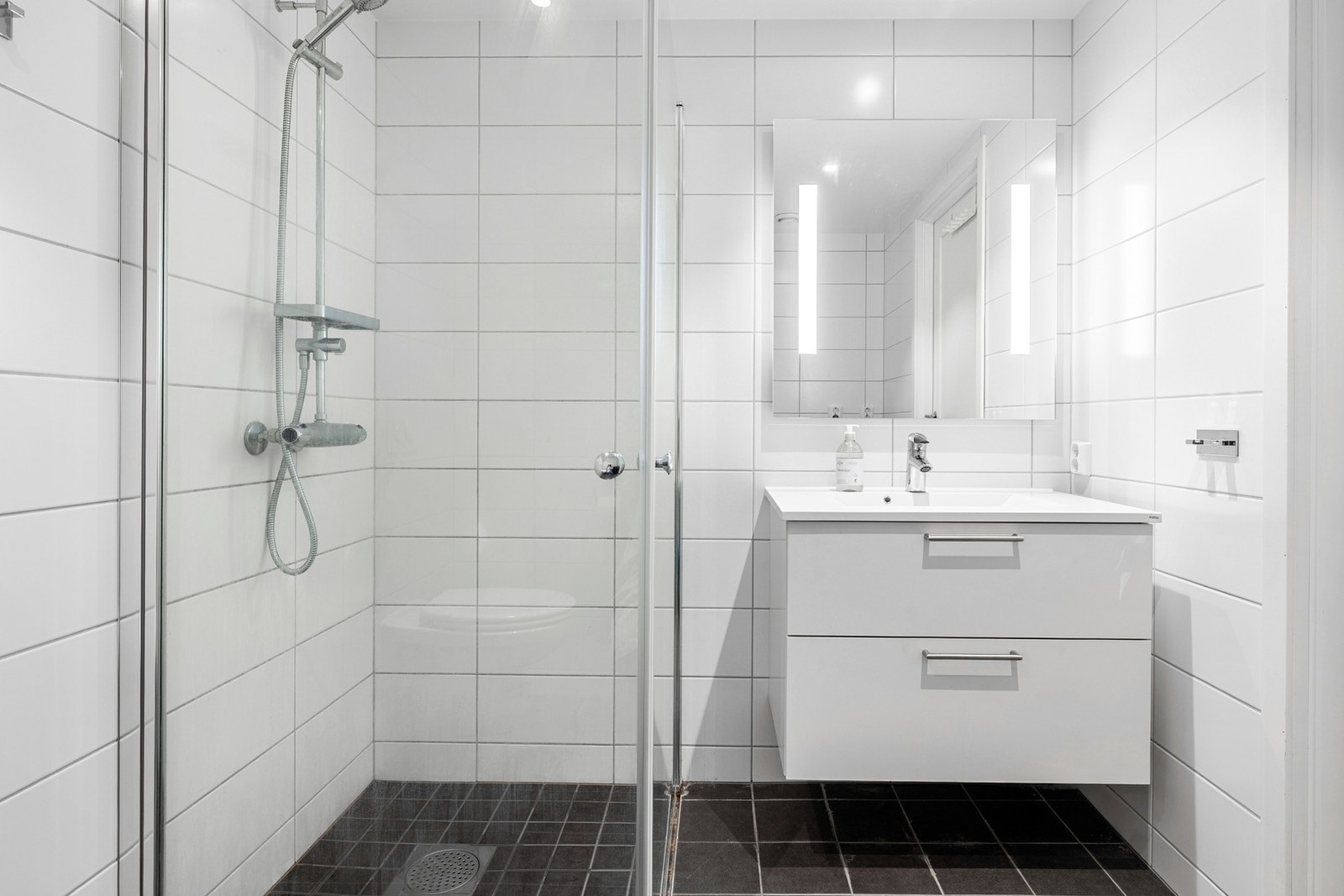 Helfliset bad med vannbåren gulvvarme, vegghengt toalett, dusjhjørne med glassdører og vask med underskap, speil og opplegg for vaskemaskin. Galleribilde