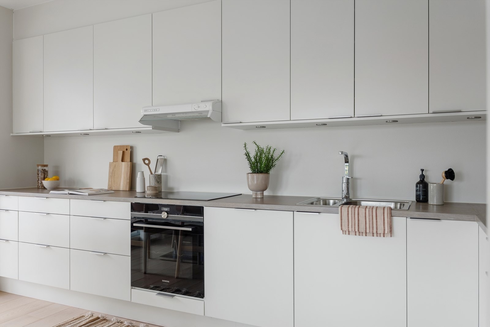 Kjøkkeninnredning med glatte folierte fronter, laminat benkeplate med nedfelt kum i rustfritt stål og ventilator tilsluttet kanal. Integrert platetopp,
stekeovn, oppvaskmaskin og kjøle/fryseskap. Galleribilde