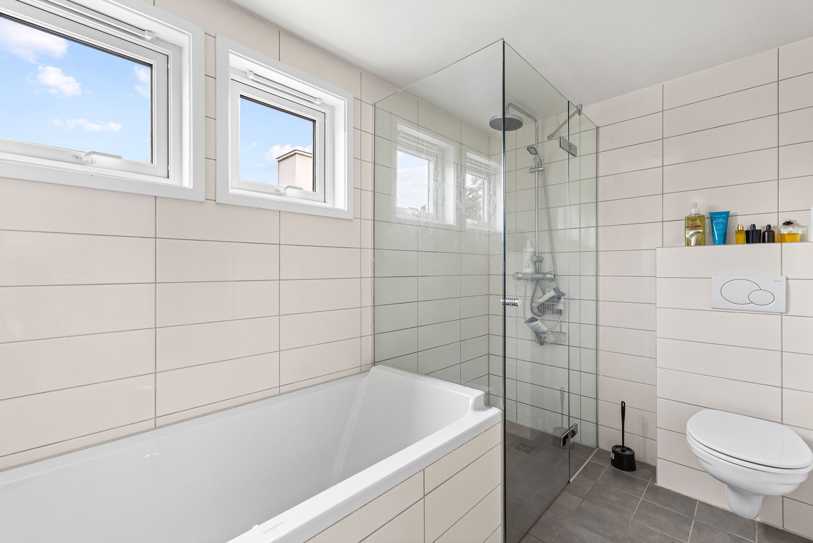 Stor dusjnisje med regndusj, hånddusj og glassvegger samt vegghengt wc med innebygget sisterne. Galleribilde