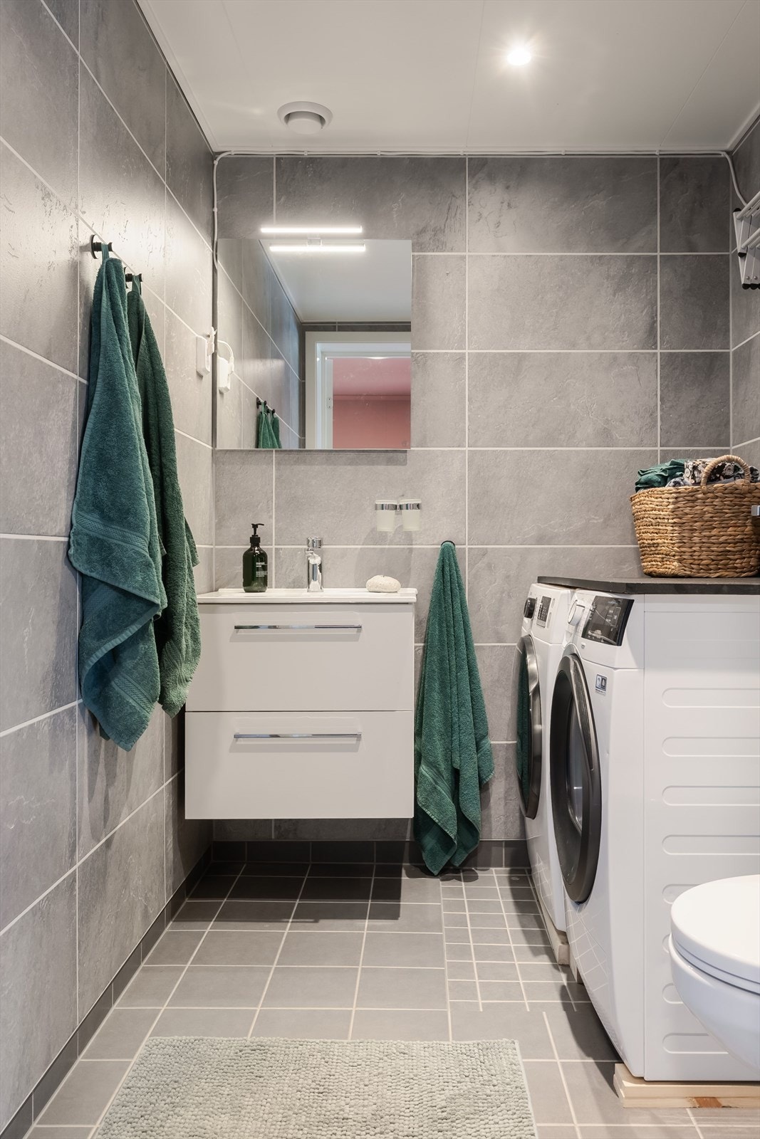 Adkomst fra hovedsoverom til moderne vaskerom med varmekabler i gulv. Baderomsinnredning, vegghengt klosett og plass til både vaskemaskin og tørketrommel. Galleribilde