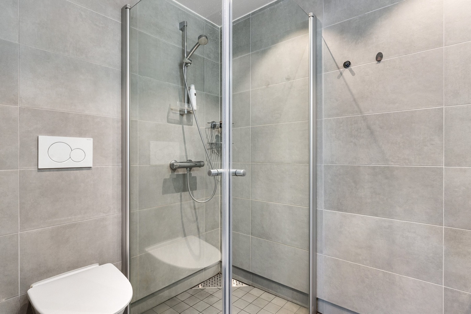 Badet har vegghengt toalett, dusjhjørne med foldedører og servant. Galleribilde