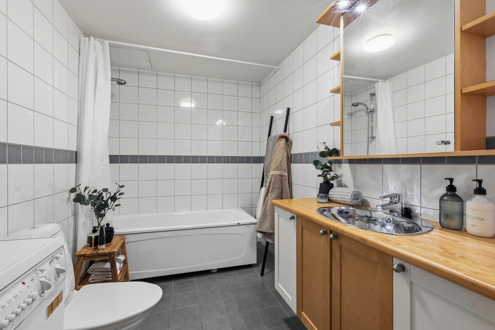Flislagt bad med en praktisk utforming med badekar, servant i innredning og toalett. Galleribilde