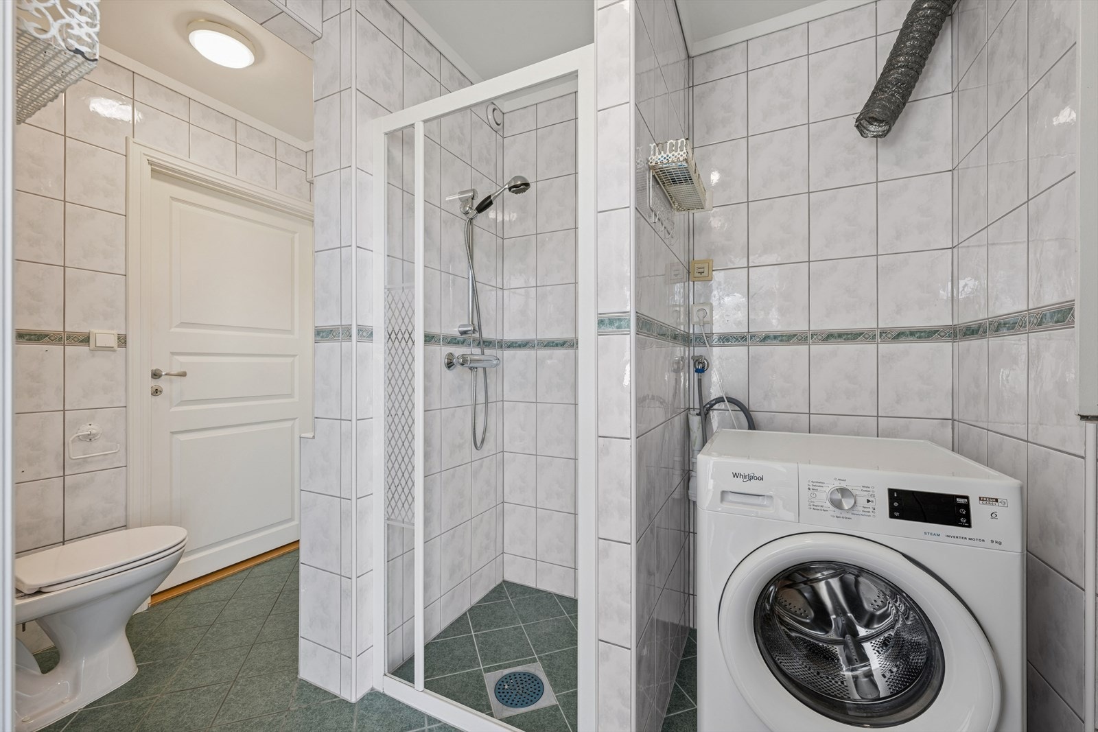Bad/vaskerommet i 1. etasje er et kombinert og funksjonelt rom med fliser på gulv og vegger, elektriske varmekabler og opplegg for vaskemaskin. Galleribilde