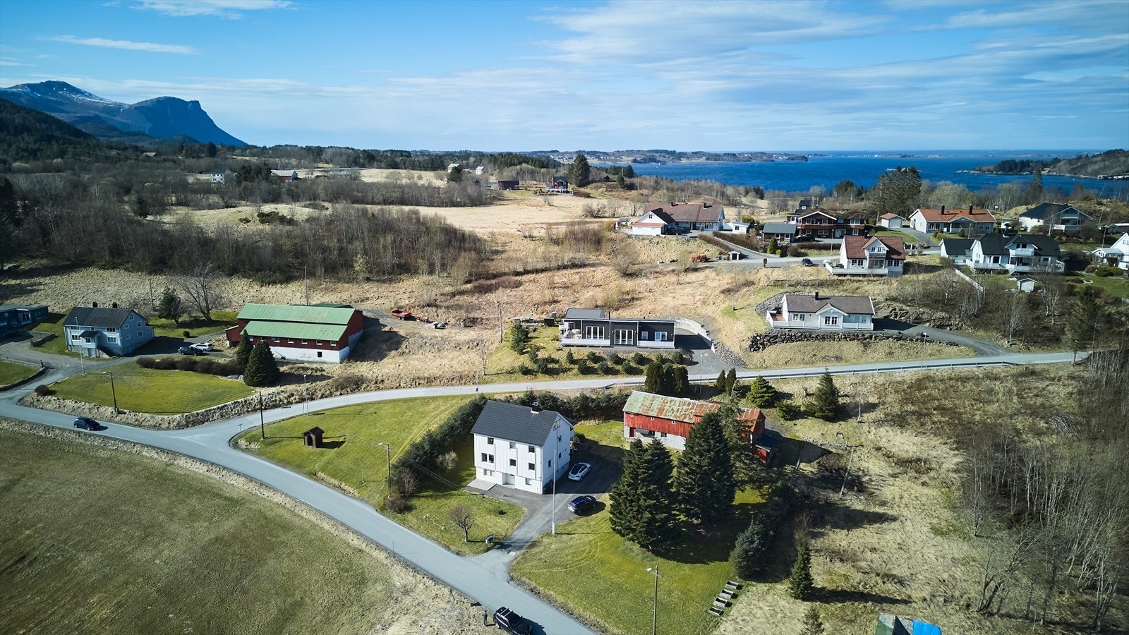 Dronebilde av eiendommen og nærområdet, tatt fra sørøst. I bakgrunnen kan man se fjelltoppene Sjurvarden og Stemshesten og den verdensberømte Atlanterhavsveien. Galleribilde