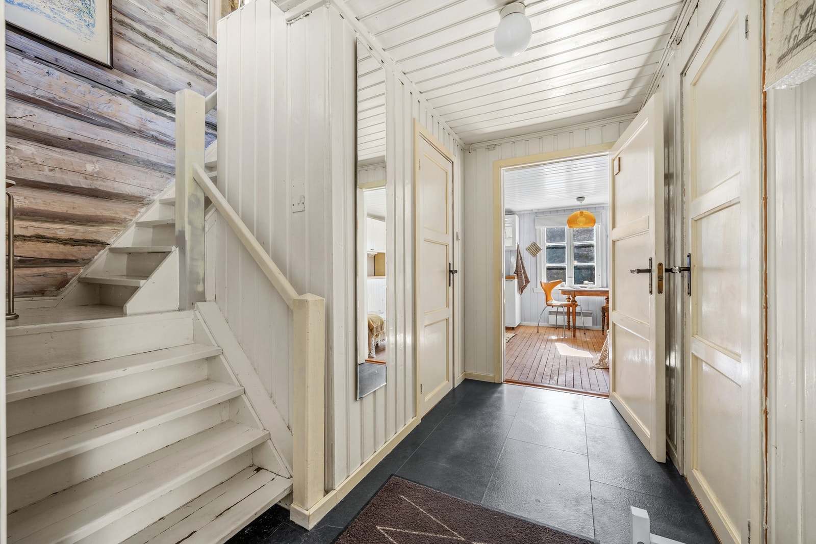 Hyggelig entre/vindfang med flisimitert belegg på gulv og malte panelvegger i kombinasjon med originale tømmervegger i trappeoppgangen. Galleribilde