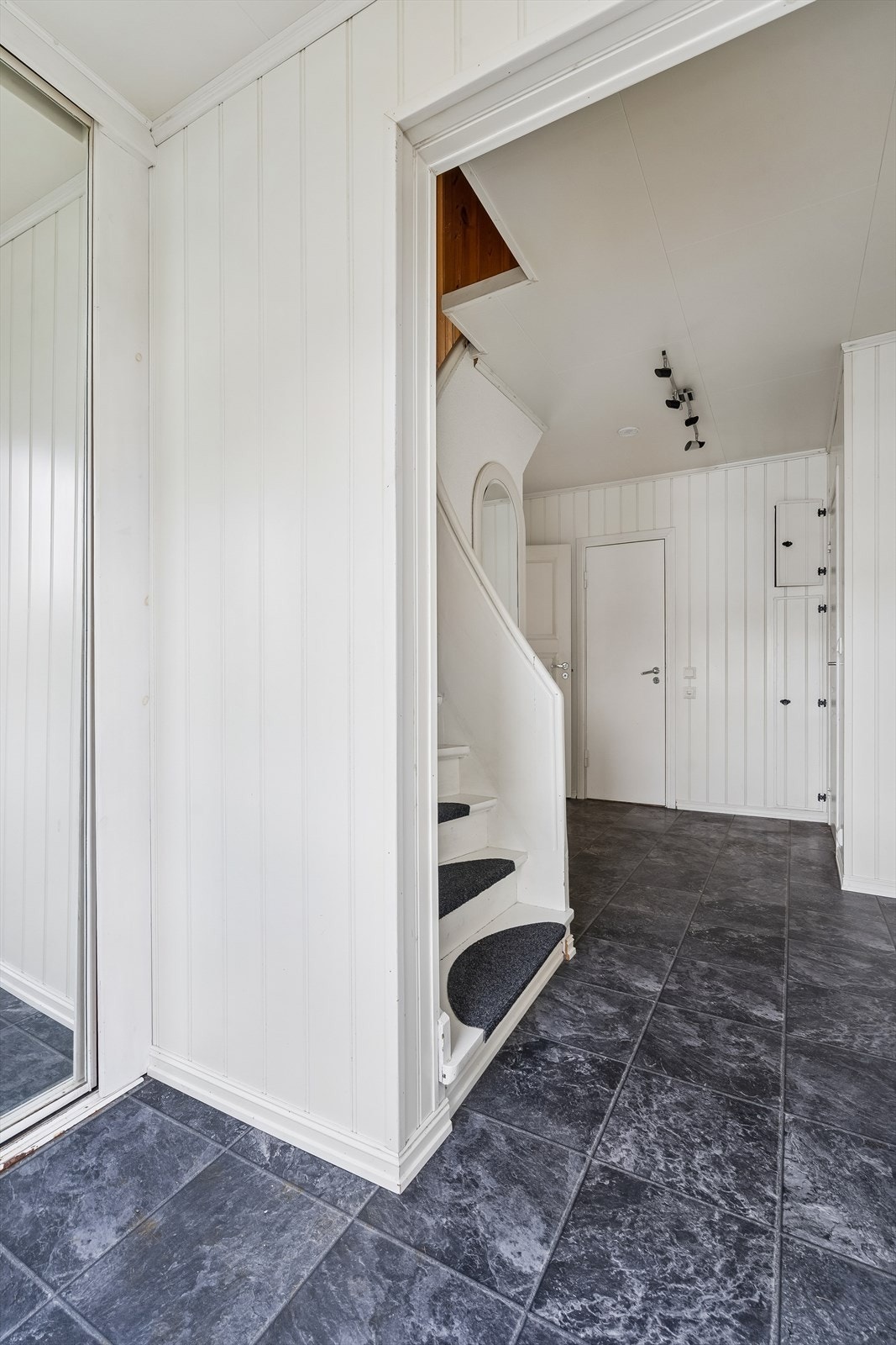 Innvendig trapp mellom etasjene er utført i malt tre og utstyrt med teppebelagte trinn. Skyvedørsgraderobe i yttergang med speilfront. Døra rett frem fører inn til boden. Galleribilde
