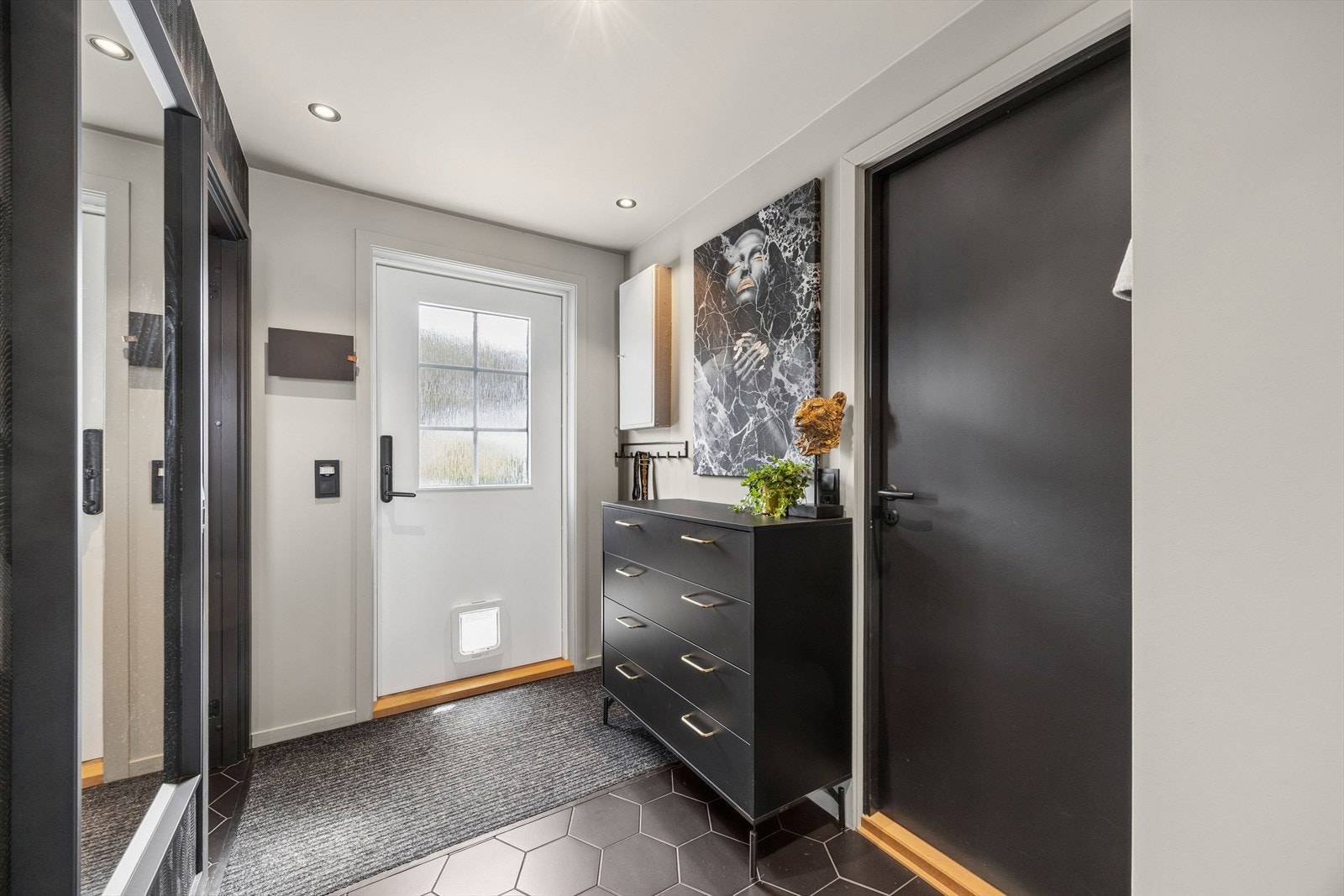 Man ønskes velkommen inn i en romslig entré som er praktisk og stilig innredet med mørke, hexagonformede fliser på gulvet og garderobe med god plass til yttertøy og sko. Galleribilde