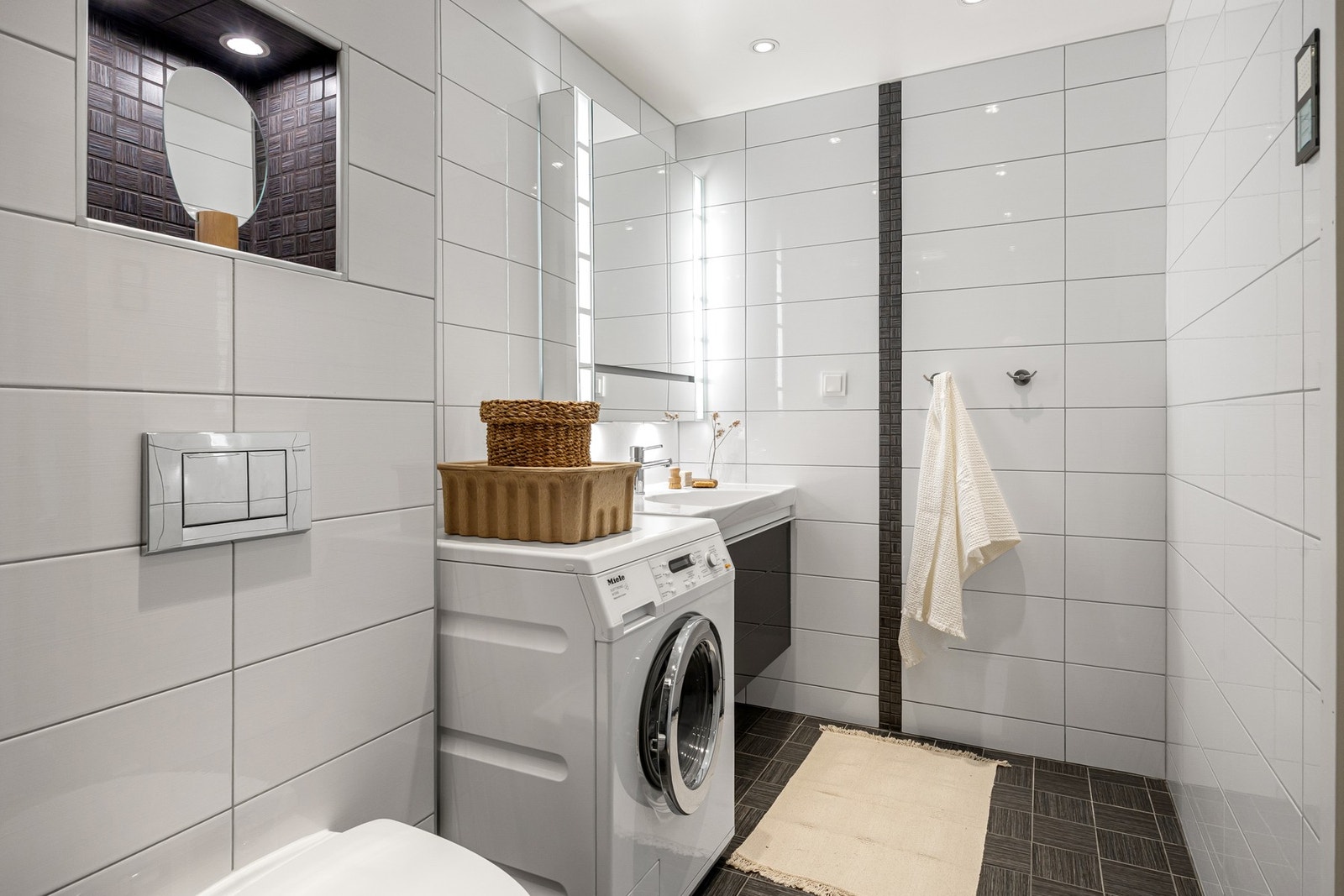 Badet har vegghengt toalett, opplegg for vaskemaskin, gulvvarme og nedsenket dusjsone med svingbare glassdører. Galleribilde