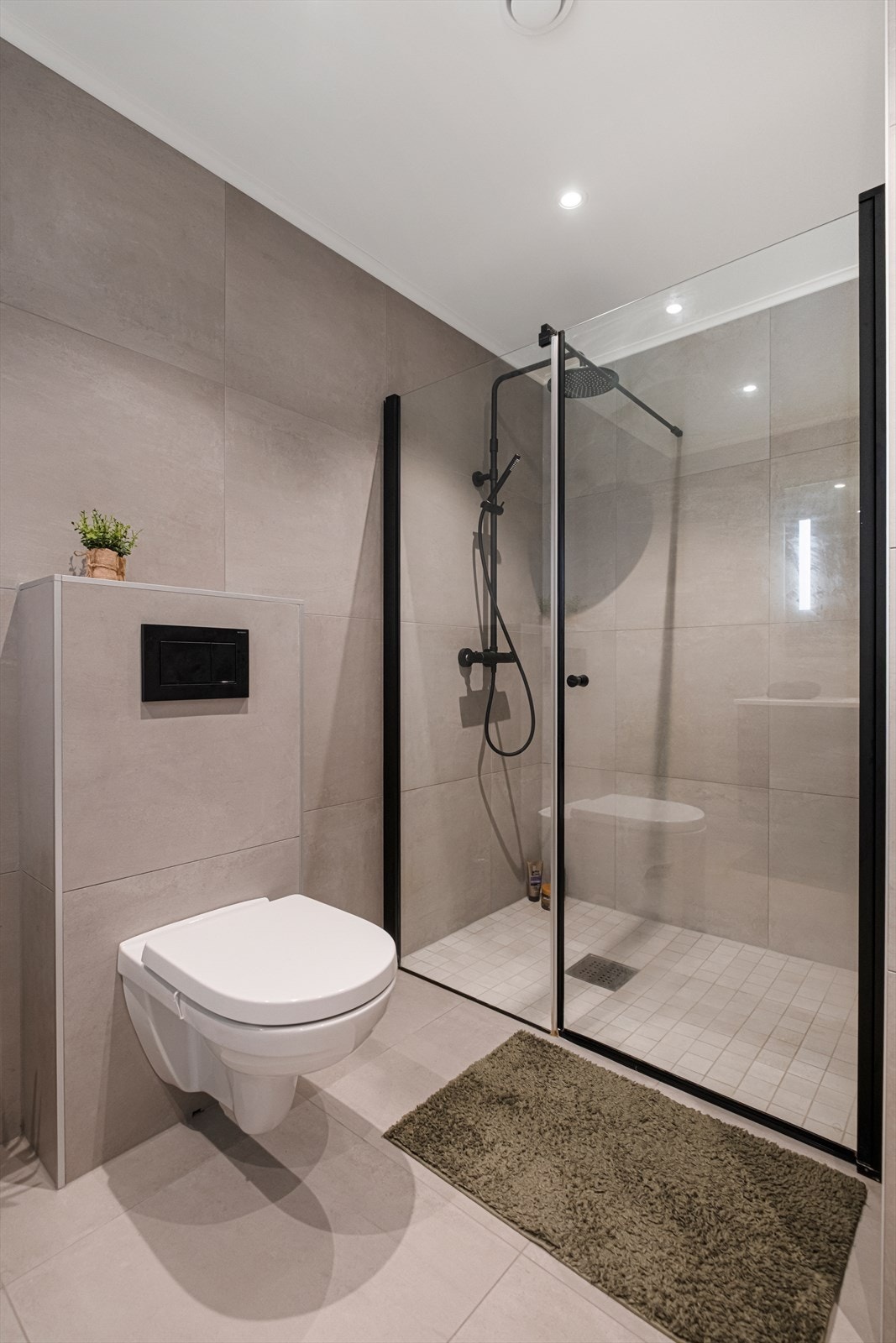 Helfliset bad med varmekabler i gulv. Badet har servantskap med heldekkende servant, speil med lys, vegghengt toalett og dusjvegger av glass Galleribilde