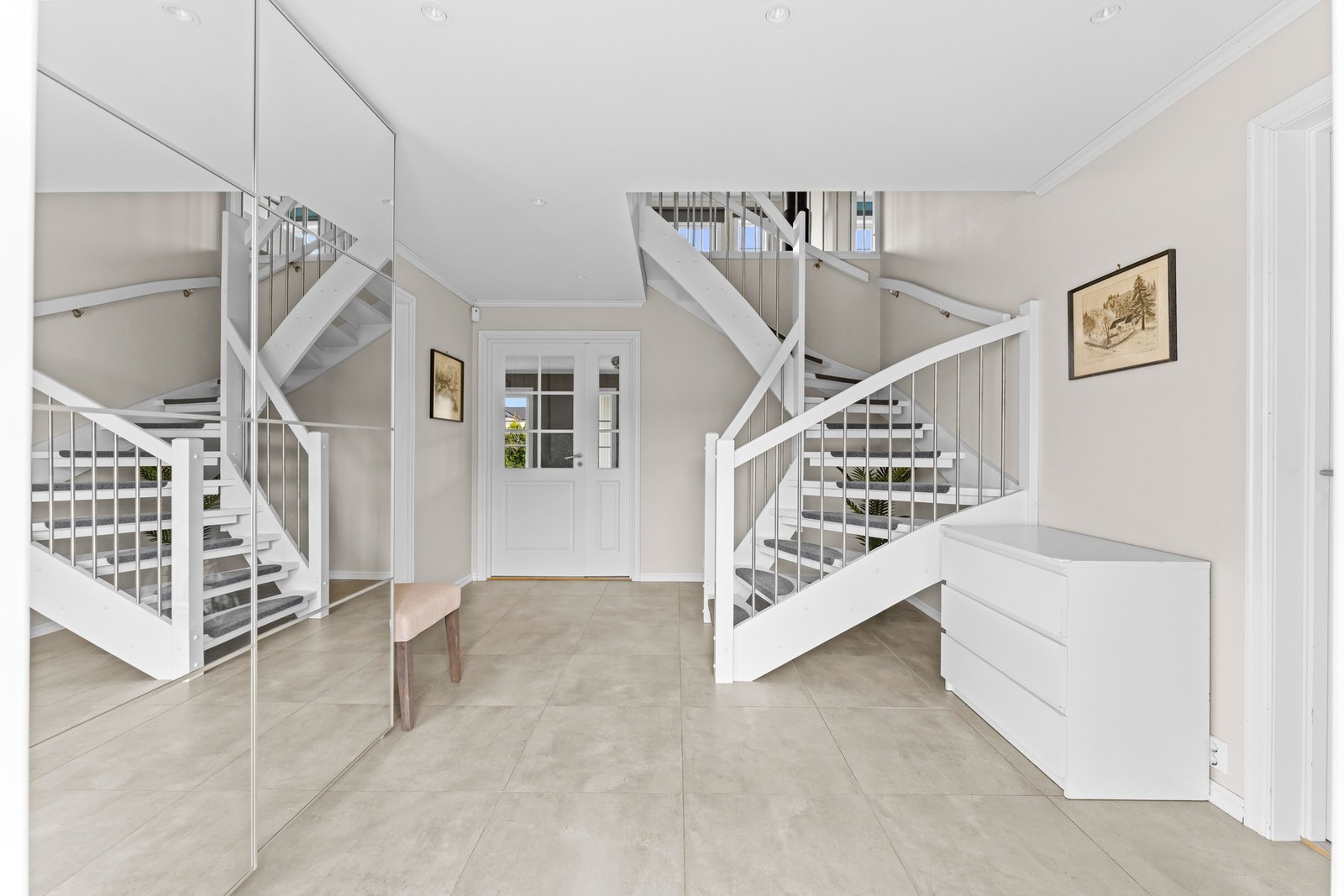 Romslig entré med store fliser på gulv med varmekabler, skyvedørsgarderobe med speilfronter og en åpen trappeløsning som gir et godt førsteinntrykk. Galleribilde