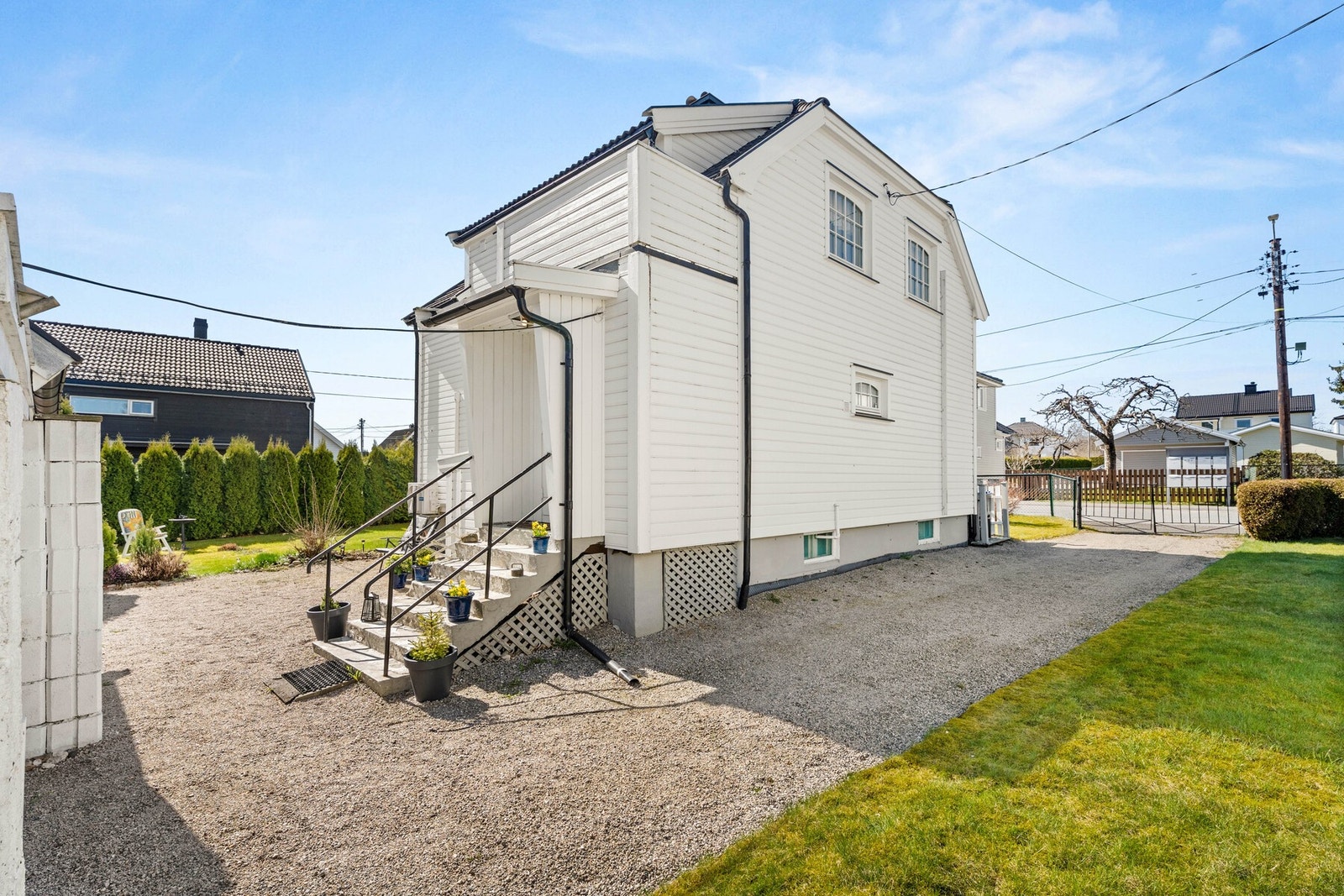 Tomten er relativ flat, det er gruset gang- og parkeringsarealer, mindre gressarealer og diverse beplantninger. Galleribilde