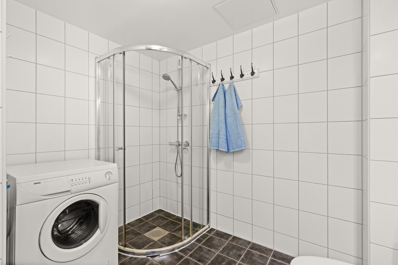 Badet er praktisk innredet med dusjnisje med glassdører og opplegg for vaskemaskin. Galleribilde