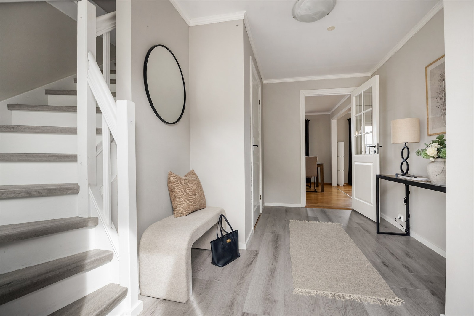 Lys og innbydende hall med nytt laminatgulv fra 2024. Trappen har laminat i trinnene og malt rekkverk. Galleribilde
