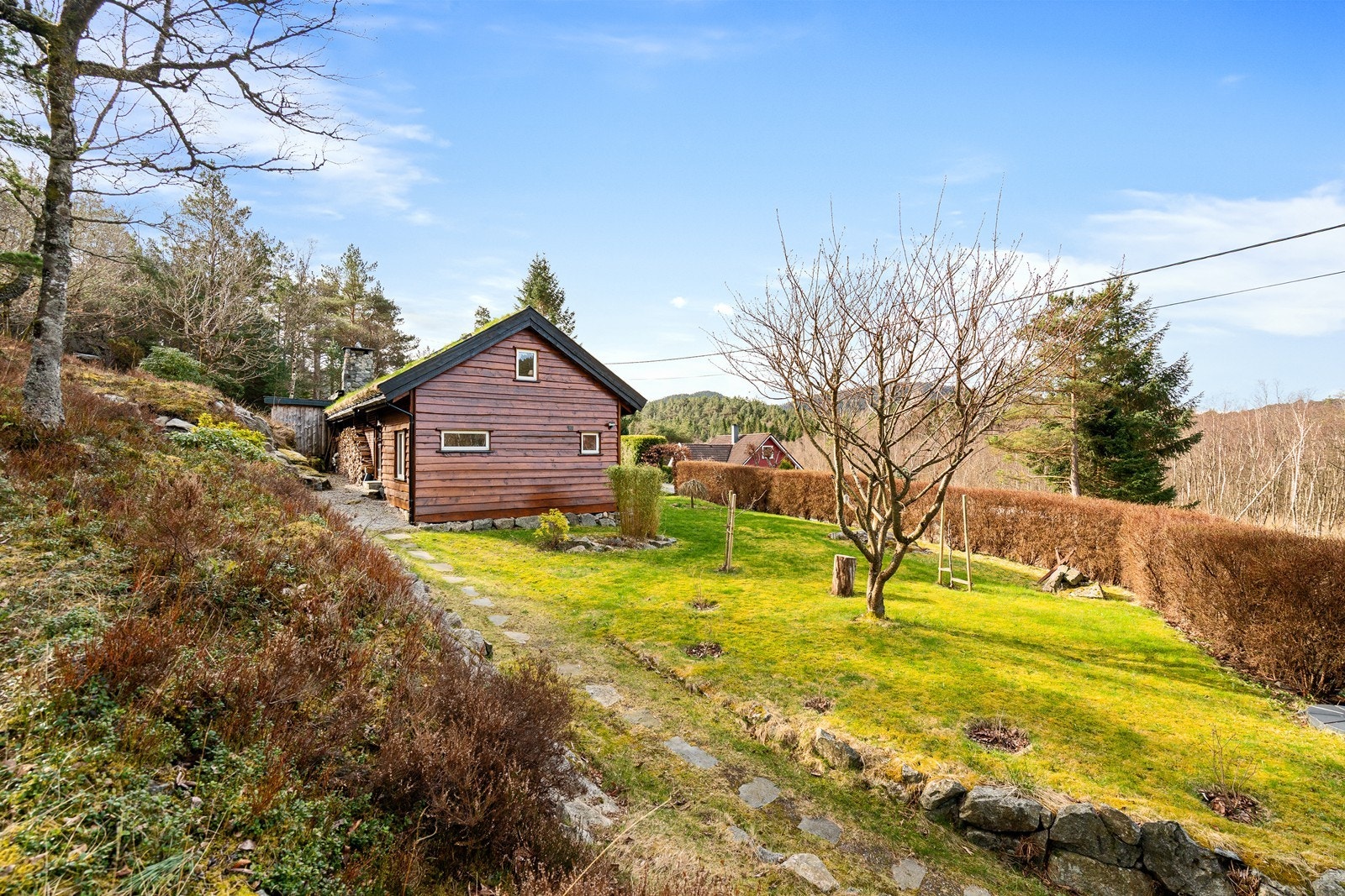 Eiendommen har et skrånende uteområde med terrasse og grøntareal, som er beplantet med plen og hekk. Galleribilde