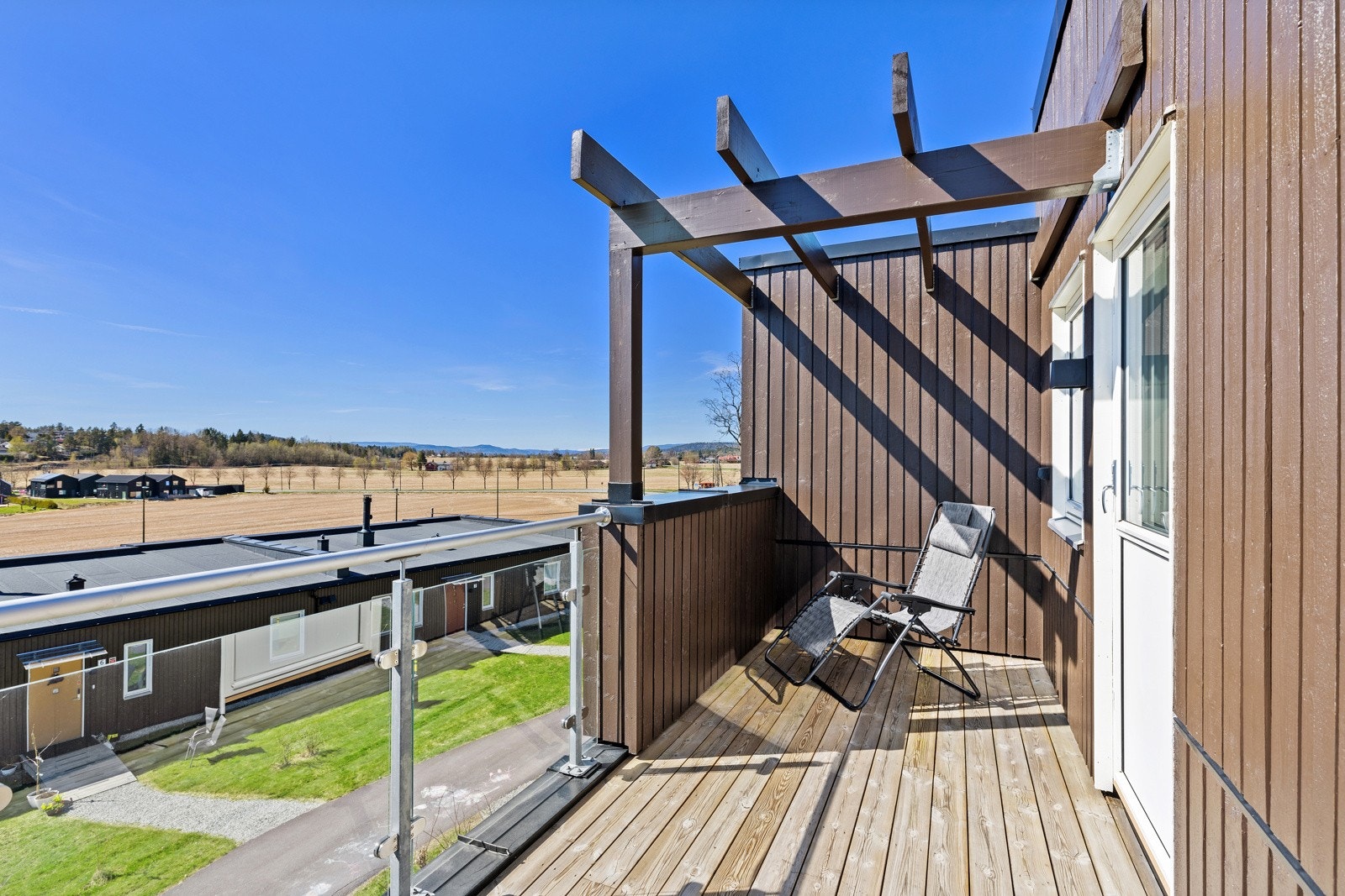 Takterrassen har pergola, glassrekkverk og fri utsikt over jorder og åsene rundt. Galleribilde