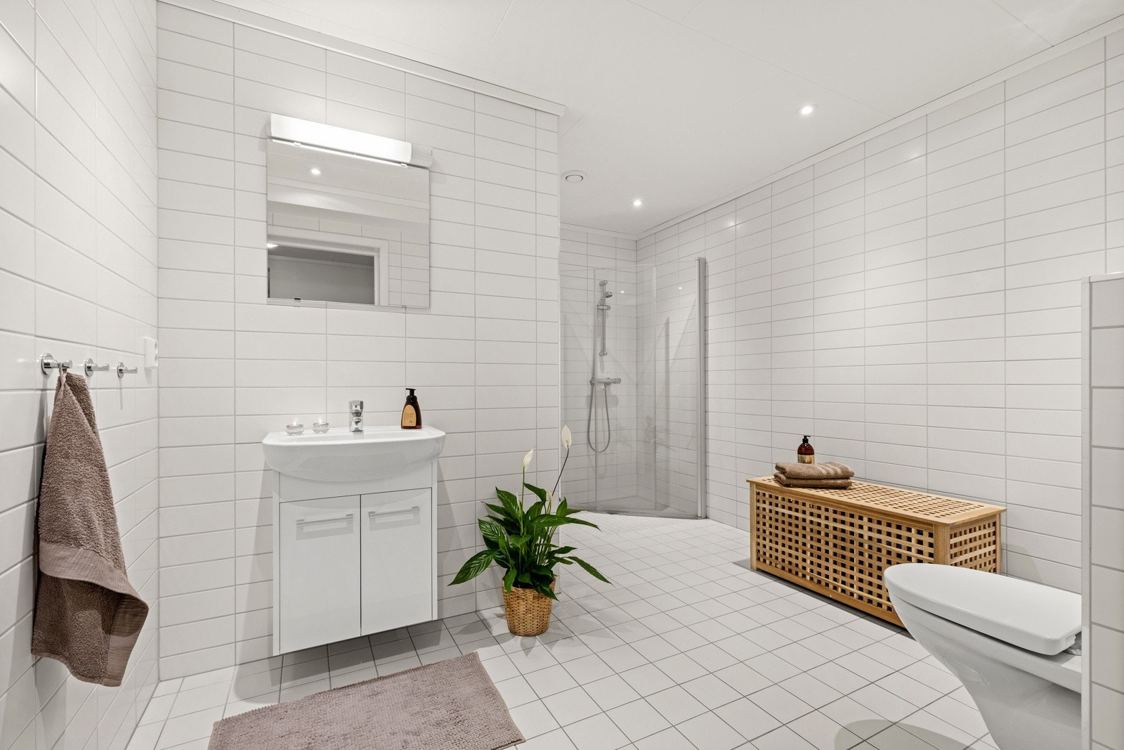 Lyst bad med dusjhjørne, toalett, servant og helflislagte flater overalt. Galleribilde