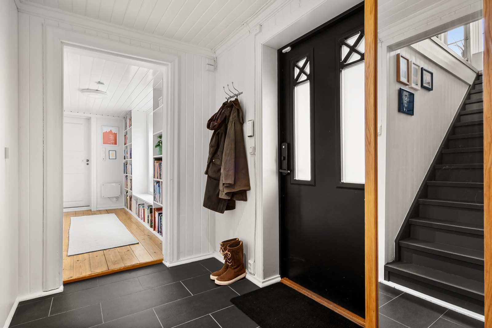 Entréen ønsker deg velkommen med lyse panelte overflater, flislagt gulv og plass til oppbevaring i en plassbygd skyvedørsgarderobe. Herfra er det videre adkomst til boligens øvrige rom og trapp til hovedetasjen. Galleribilde