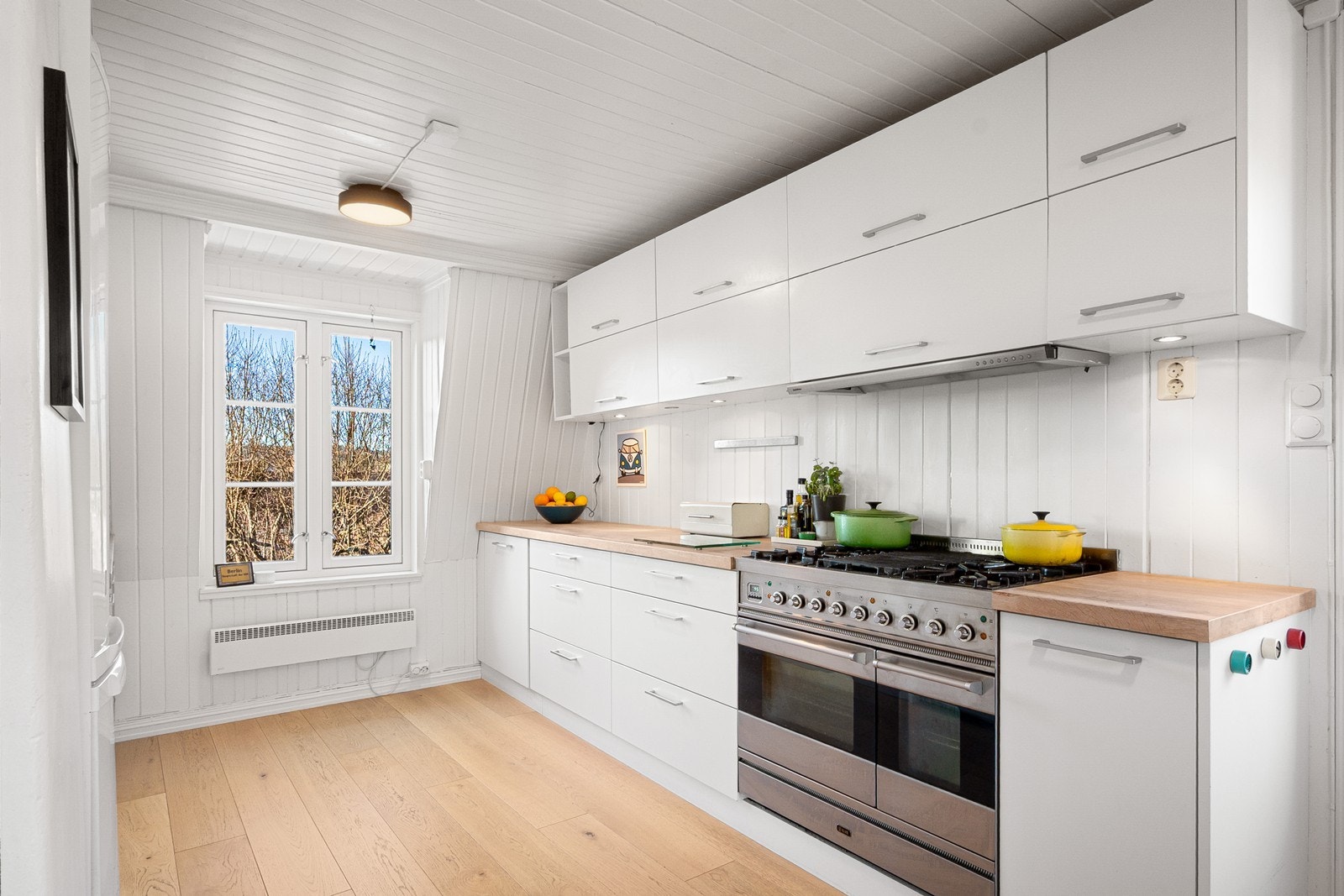 Kjøkkenet er romslig og funksjonelt utformet med skapinnredning med slette fronter i malt MDF og benkeplate i heltre eik med benkebeslag i kompositt. Galleribilde