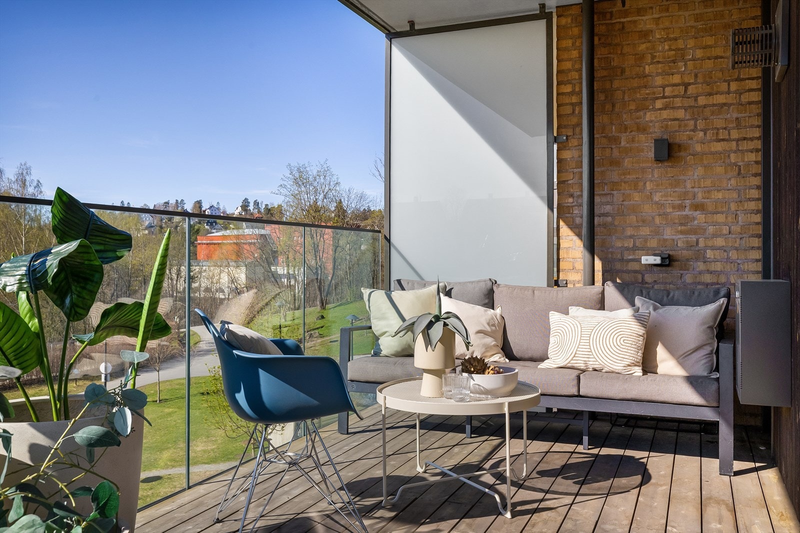 Hjørnebalkong med lekkert glassrekkverk, terrassebord og bred skyvedør inn til stue. Galleribilde