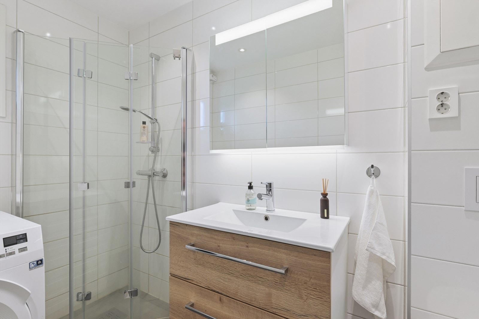Badet er utstyrt med opplegg til vaskemaskin og tørketrommel, servant, dusjhjørne og vegghengt toalett Galleribilde