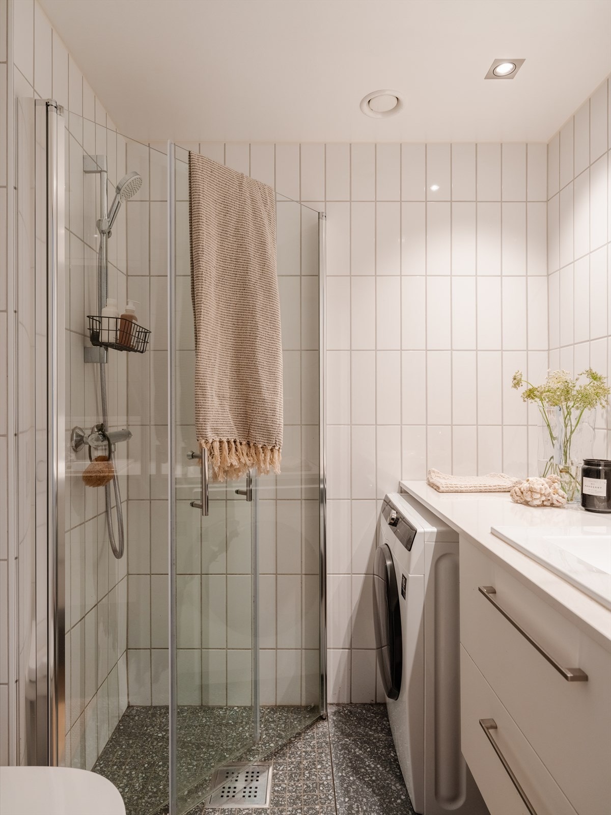 Stilrent bad med nedsenket dusjsone avgrenset med glassfelt, flislagte overflater, elektrisk gulvvarme, vegghengt toalett og servant med skuffeseksjon. Galleribilde