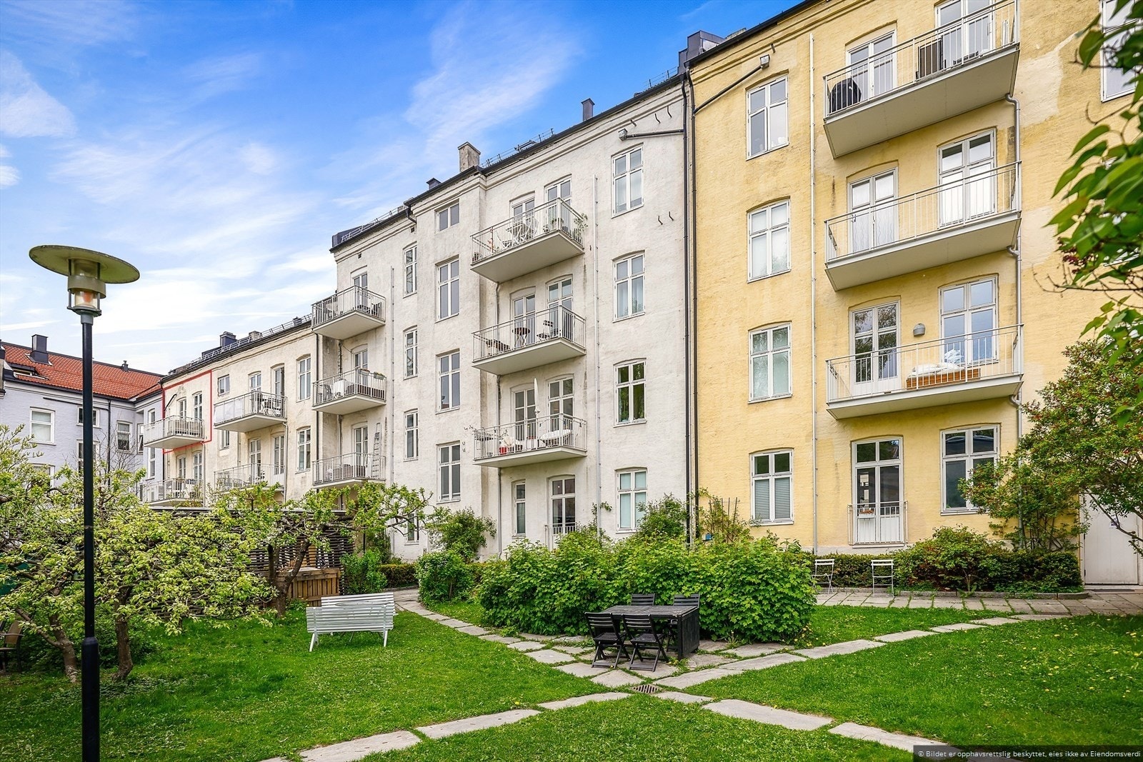 Flott og frodig bakgård med gressplen, sitteplasser og annen beplantning. Galleribilde