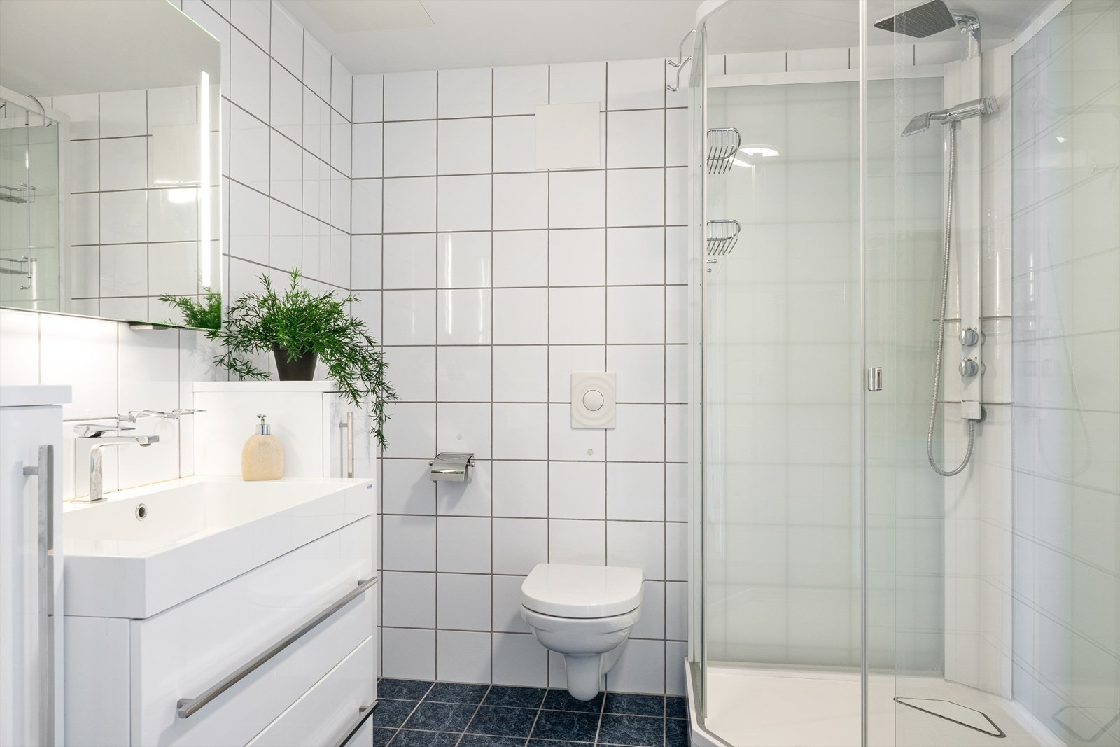Badet er helfliset og har et stilrent uttrykk. Det er innredet med dusjkabinett, vegghengt servant med underskuffer og toalett. Galleribilde