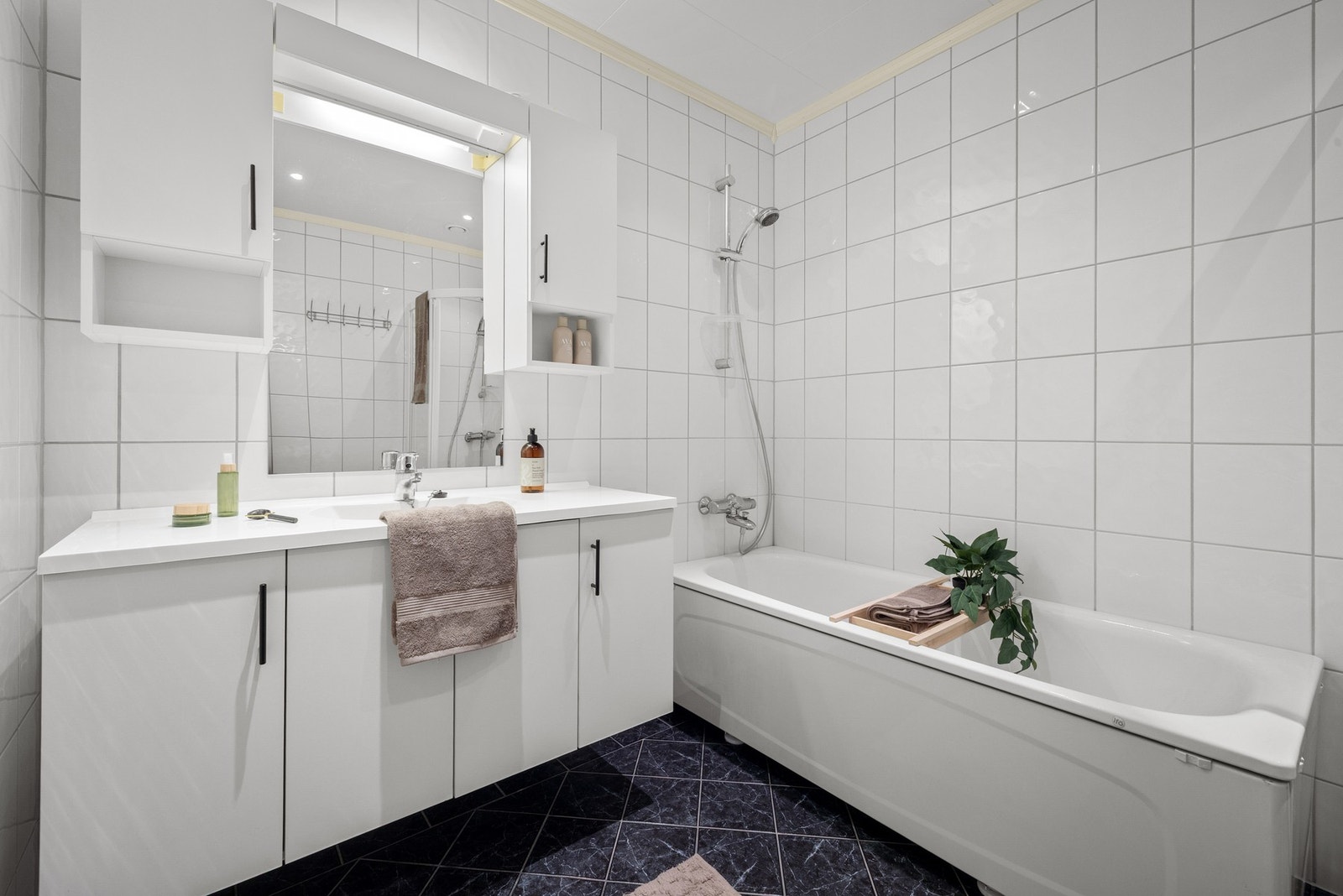 Badet er på 5,7 kvm og er helfliset med lyse og tidløse fliser på veggene, og mørke fliser på gulvet. Galleribilde