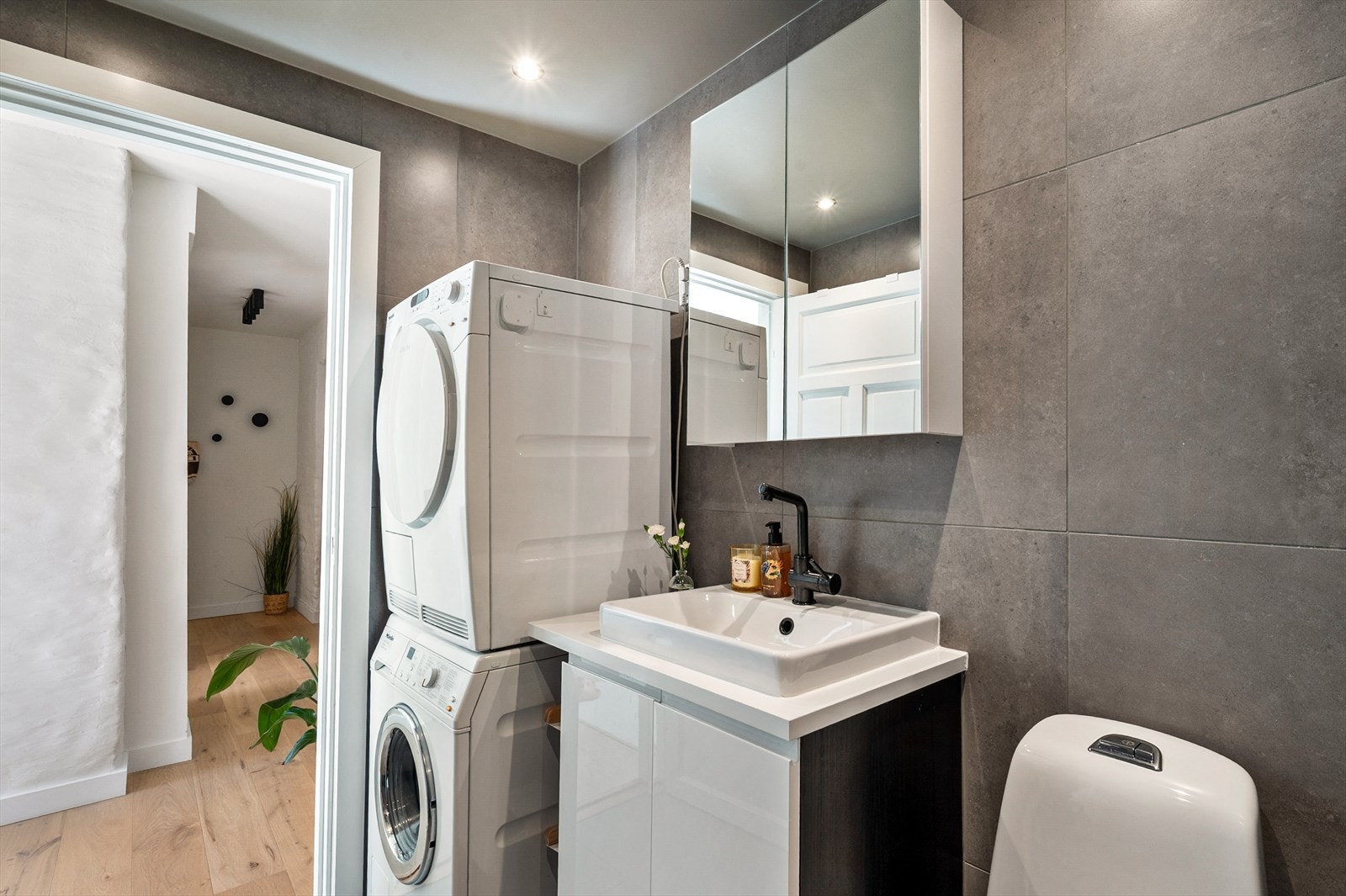 Badet er utstyrt med en romslig dusjnisje med glassdør, toalett, moderne servantskap med speil samt opplegg for vaskemaskin og tørketrommel. Galleribilde