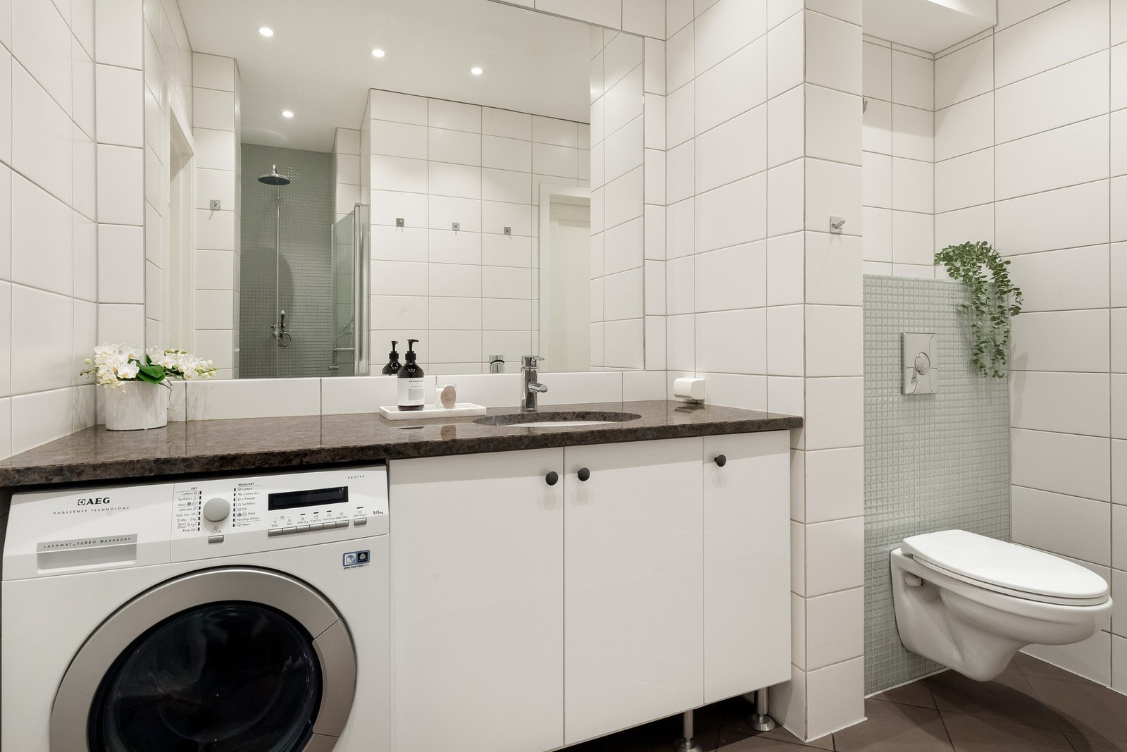 Pent flislagt baderom fra 2009 med gulvvarme, innfelte downlights og stort speil, samt vegghengt toalett, servant i granitt benkeplate og plass for vaskemaskin (medfølger). Galleribilde