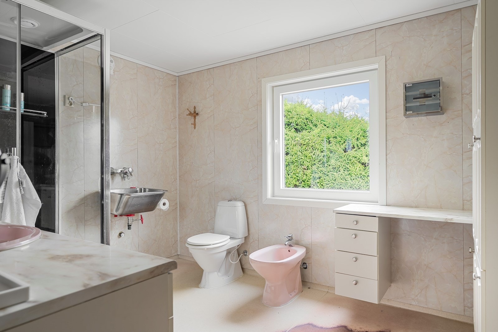 Badet har belegg på gulv med gulvvarme samt våtromsplater på vegger og er utstyrt med dusjkabinett, mekanisk avtrekk, opplegg for vaskemaskin, skyllekum, servant, servantskap og WC Galleribilde